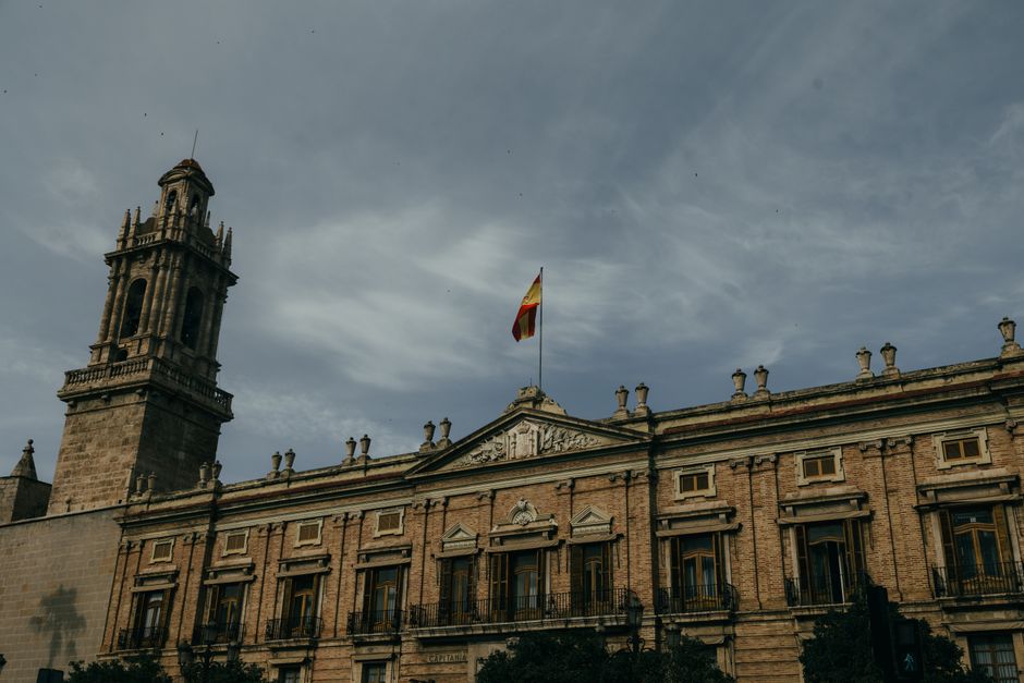 Un edificio histórico adornado con una bandera española bajo un cielo nublado en Valencia, España.