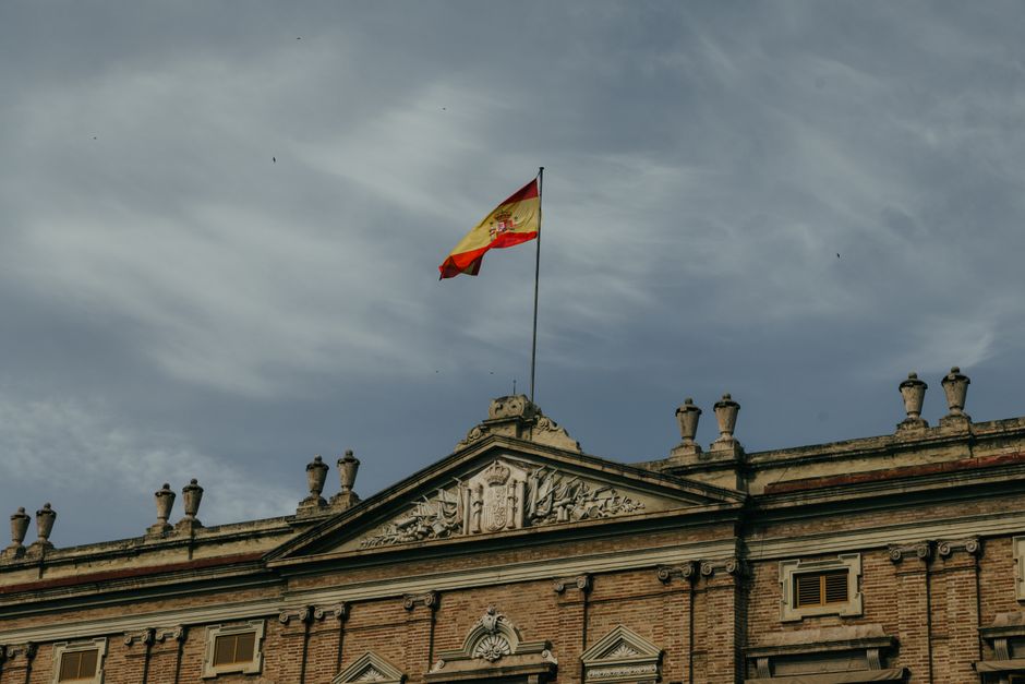 Un edificio histórico en Valencia con la bandera española ondeando contra un cielo nublado, que muestra la arquitectura clásica.