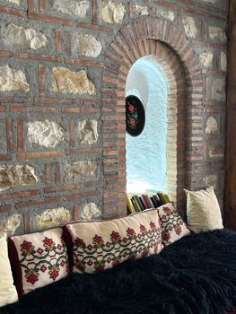 Inviting alcove with a stone wall, embroidered pillows, and an arched window, featuring a rustic interior design.