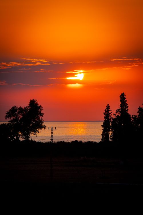 Free Breathtaking sunset with vibrant orange sky reflecting over a serene lake. Stock Photo