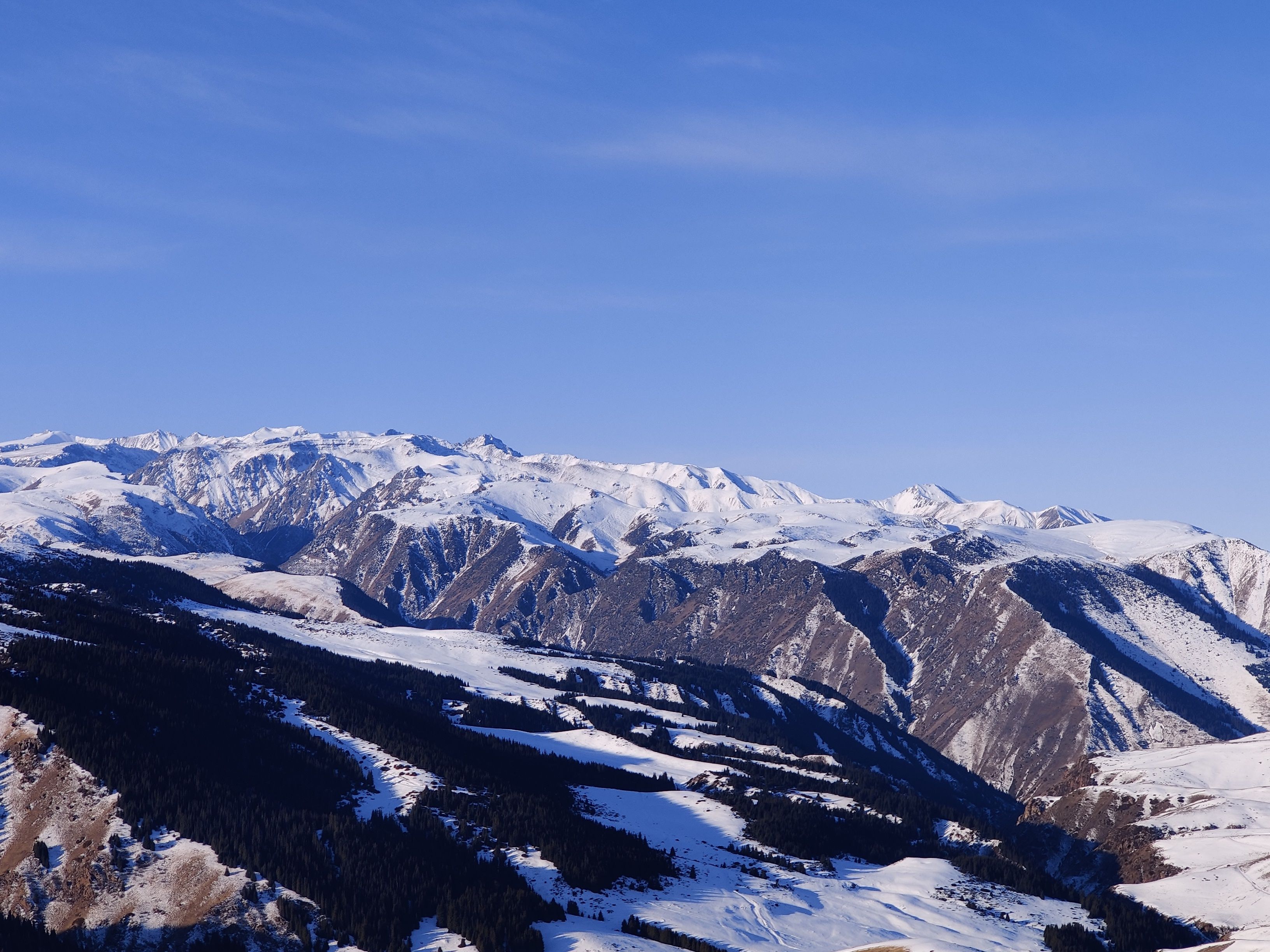 Breathtaking view of snowy mountains under a clear blue sky in Almaty Region, Kazakhstan.