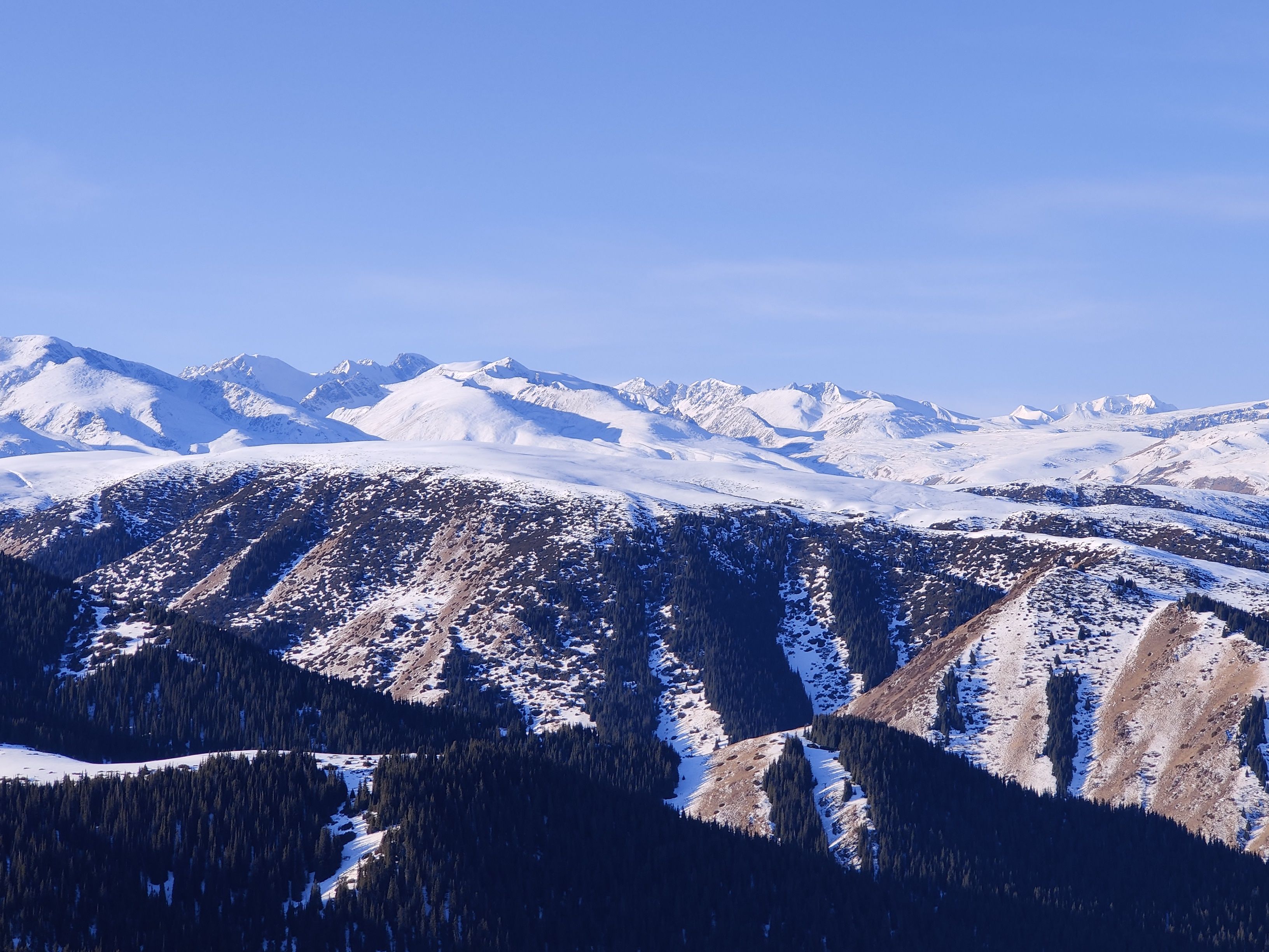 Breathtaking view of snow-covered mountains in the Almaty region of Kazakhstan, under a clear blue sky.