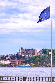 European Union flag fluttering against Stockholm's historic skyline, showing classic architecture by the waterfront.