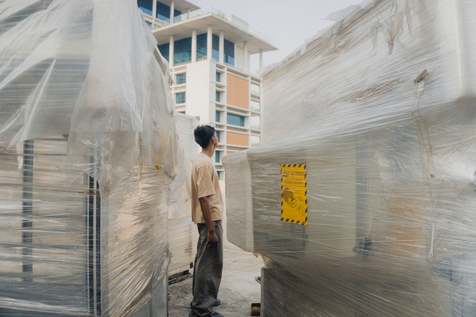 A worker stands between wrapped machinery on a construction site in Dhaka, Bangladesh.