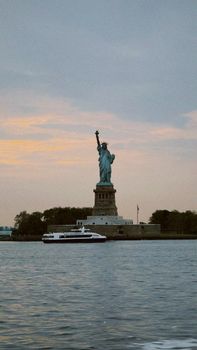 Scenic view of the Statue of Liberty against a sunset sky, featuring a nearby ferry on the water.