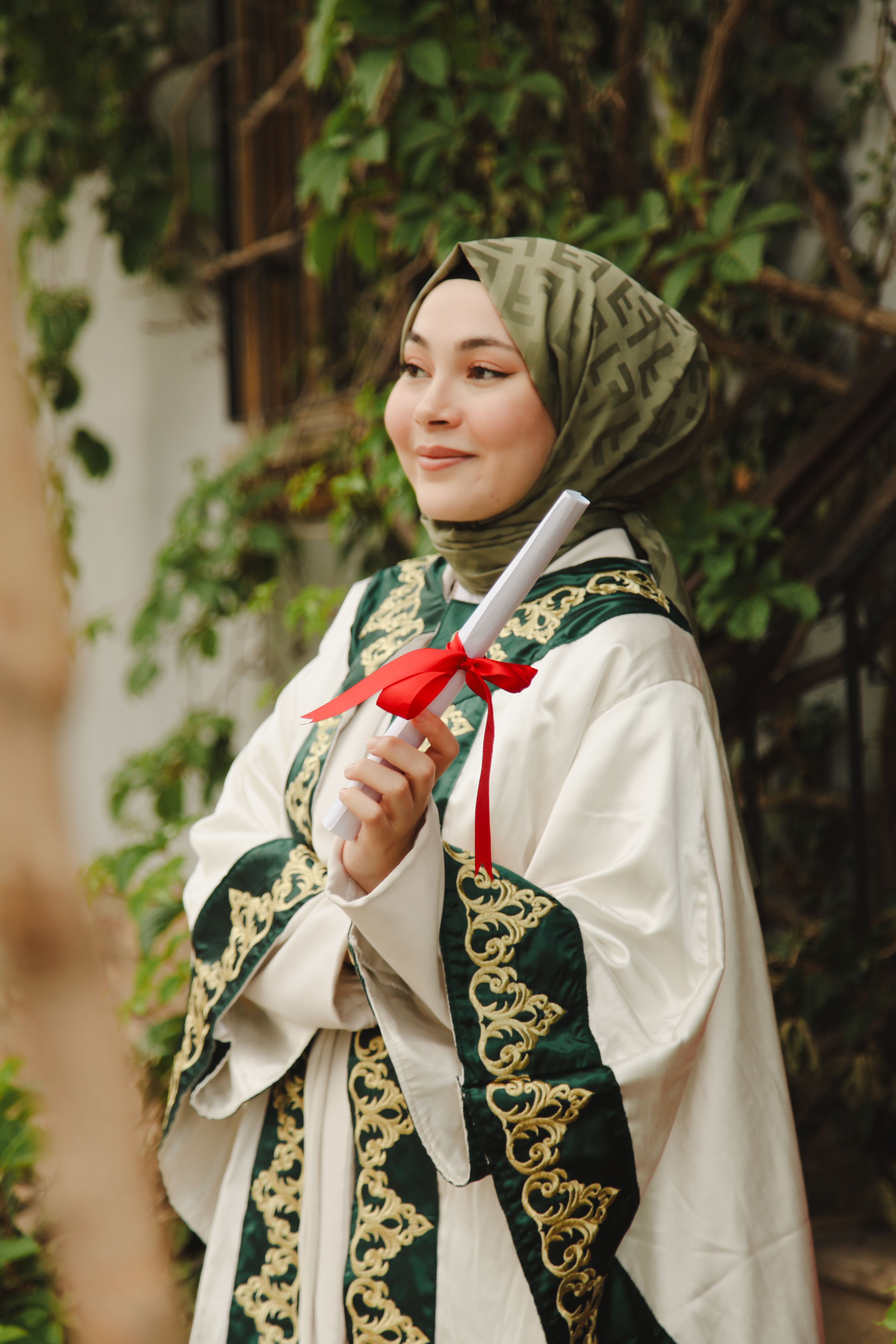 A young woman celebrates her graduation dressed in a traditional gown, holding a diploma.