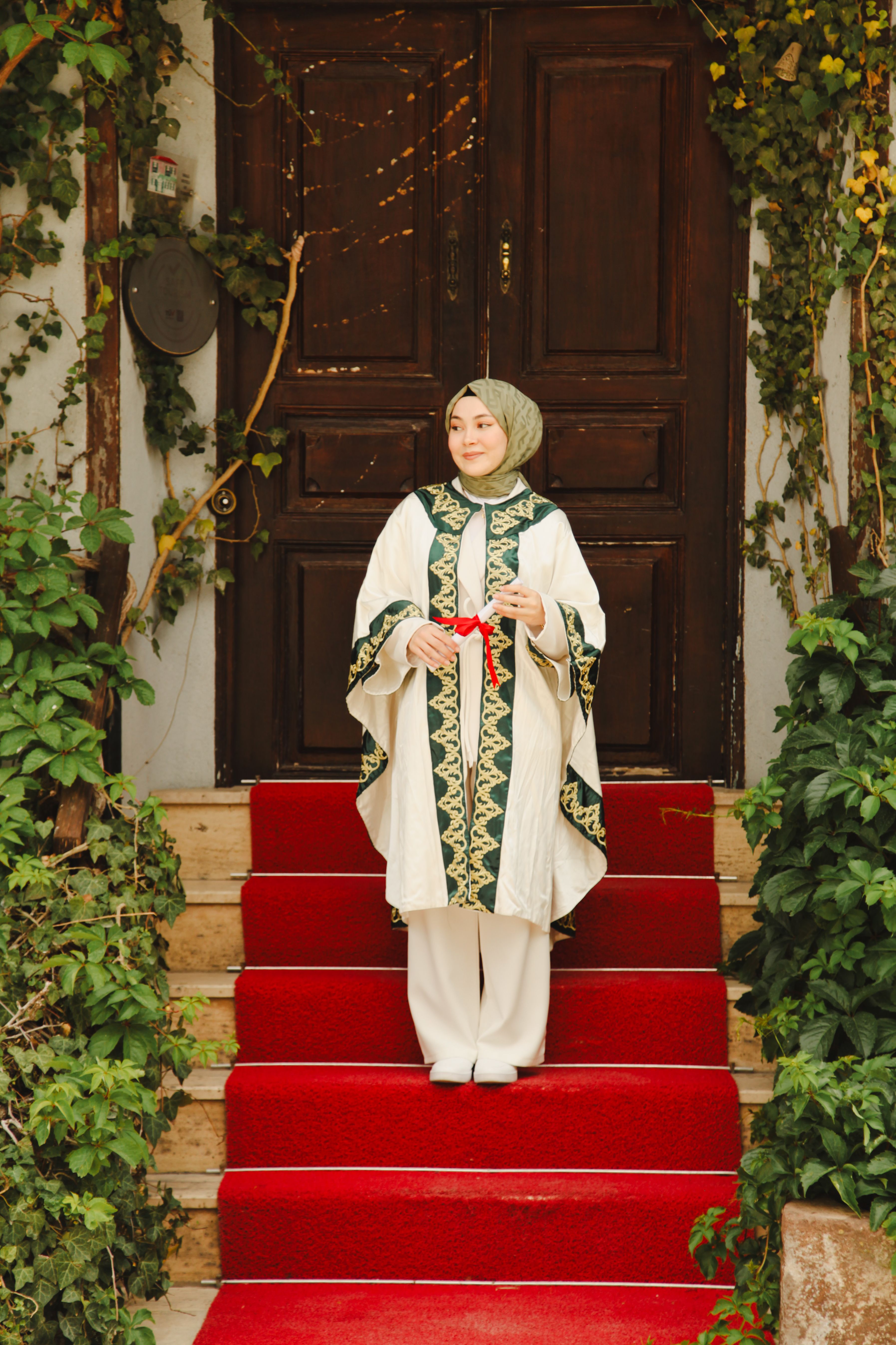 Woman in traditional attire stands on red carpet outside decorative wooden door.