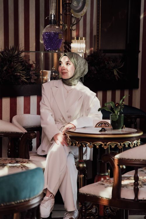 Free Elegant woman in a hijab sitting in a chic cafe with a serene expression, surrounded by vintage decor. Stock Photo