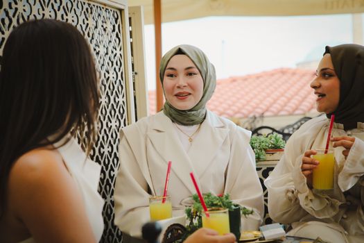 Three women chatting and enjoying drinks outdoors, showcasing friendship and leisure.