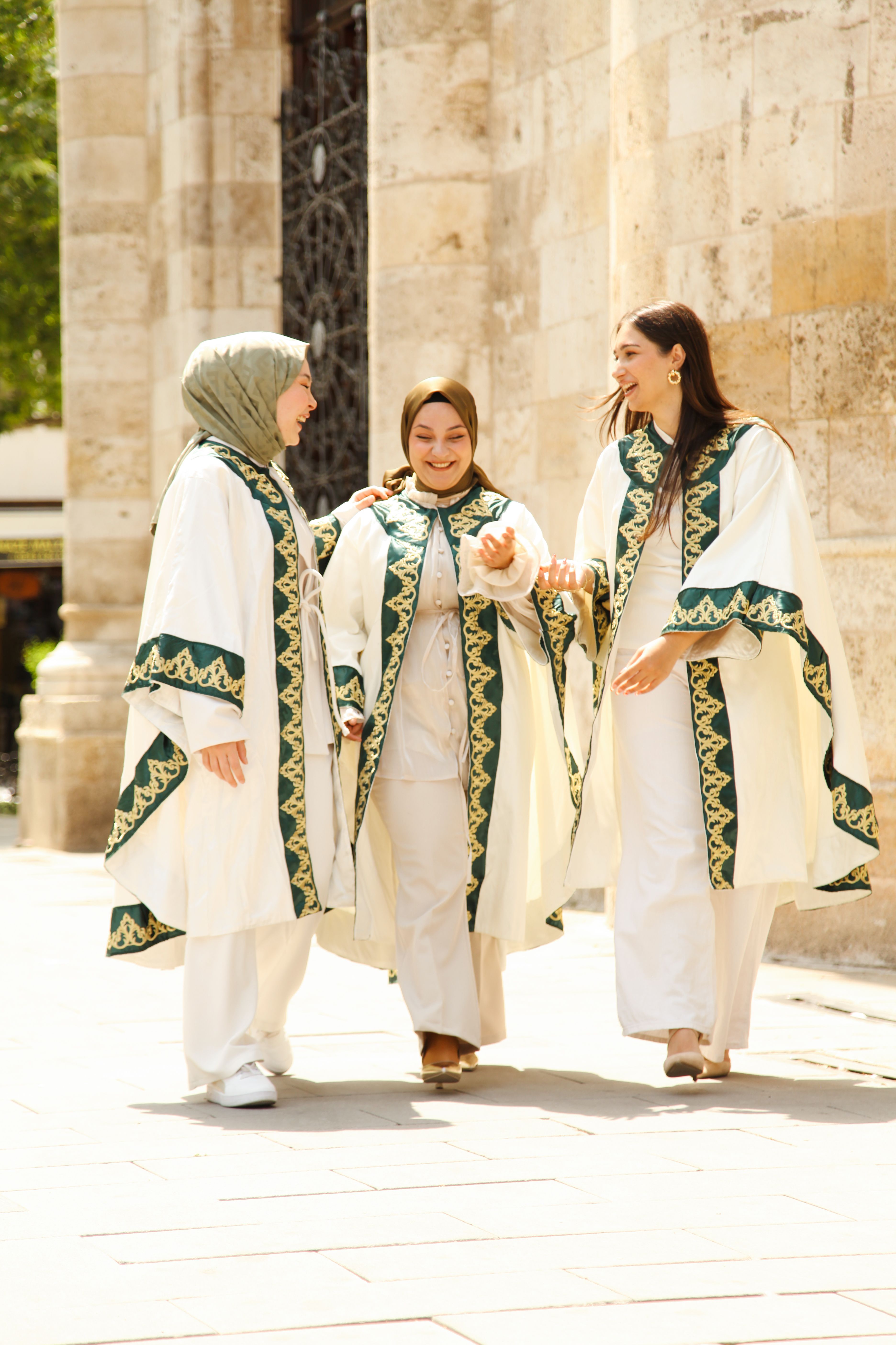 Three women in traditional Islamic clothing walking and smiling outdoors on a sunny day.