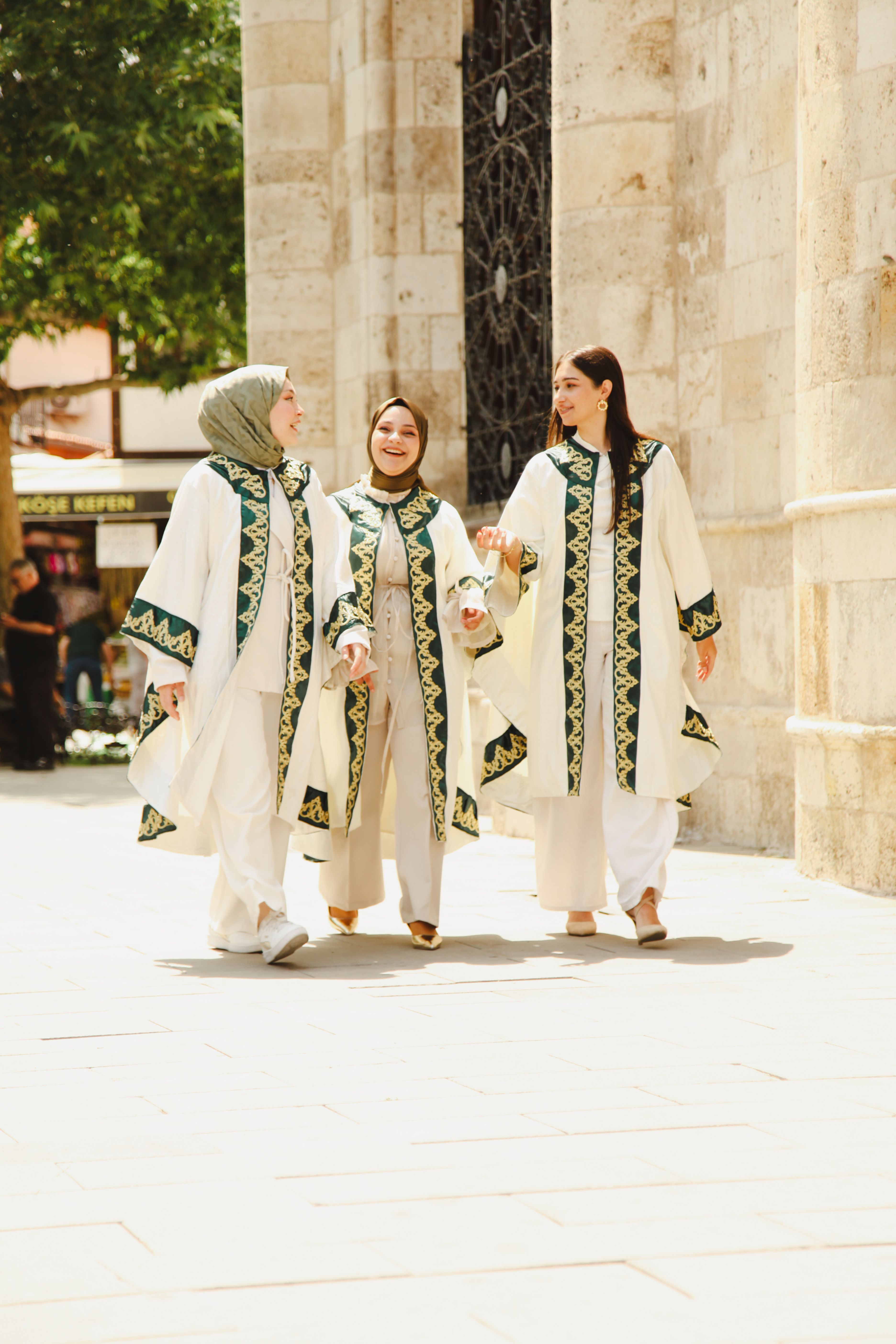 Three women in cultural attire walking together on a sunny day.