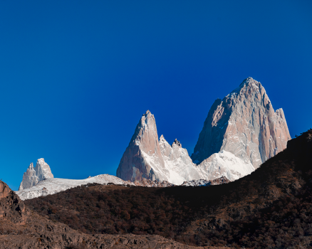 A stunning view of Mount Fitz Roy's snowy peaks in Patagonia, Argentina, under a vibrant blue sky.