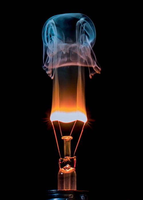 Free Dramatic image of a light bulb filament burning with vibrant smoke against a dark background. Stock Photo