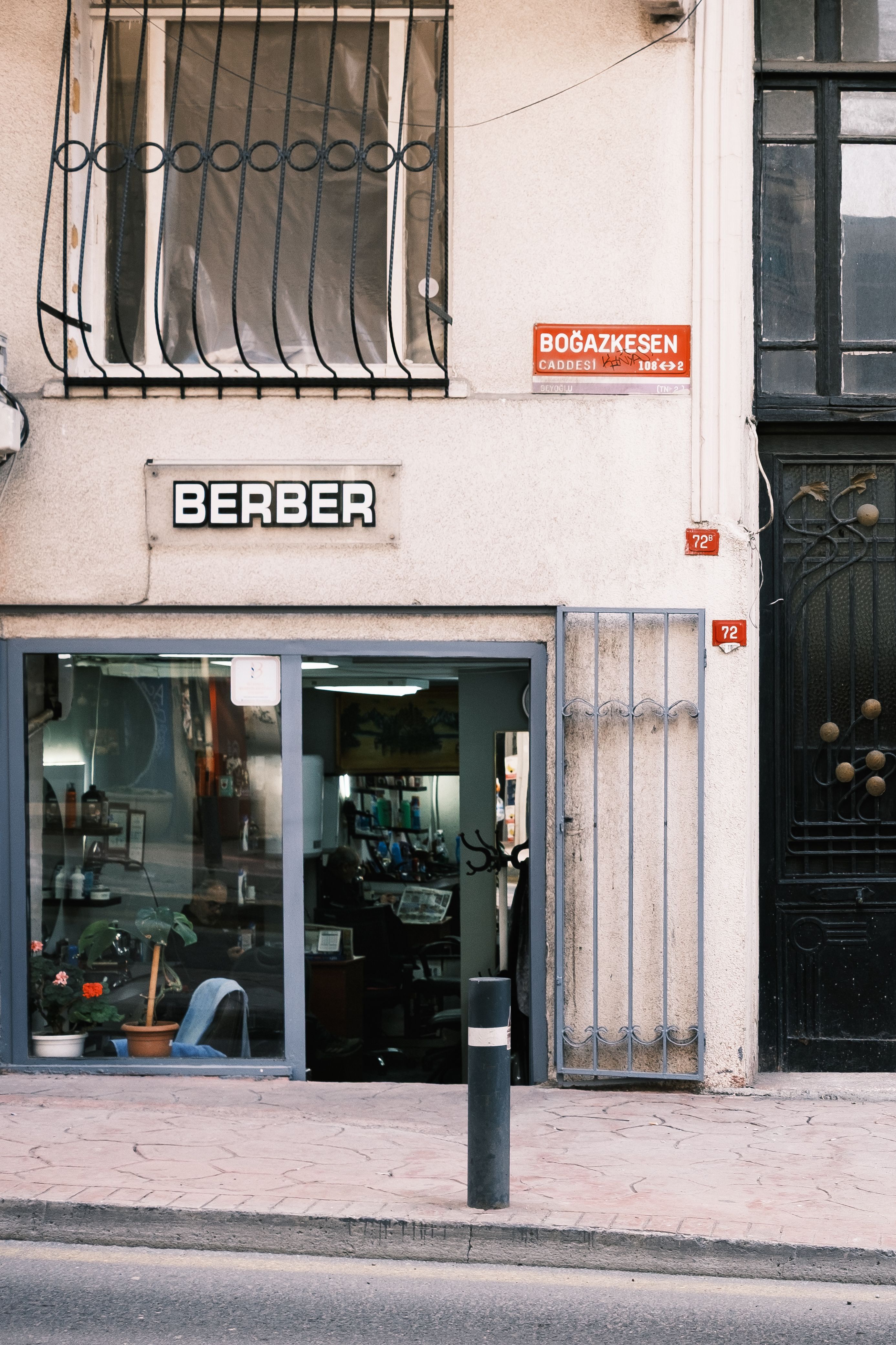 A quaint barbershop entrance on a city street corner with signage and flower pots.