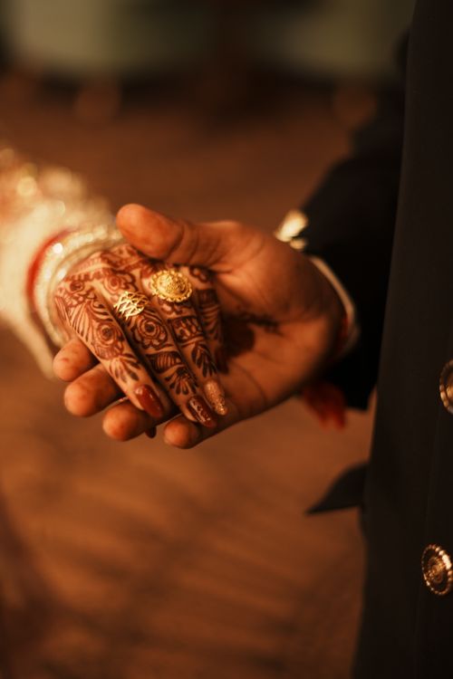 Free Close-up of a couple holding hands, showcasing intricate henna designs and bridal jewelry at an Indian wedding. Stock Photo