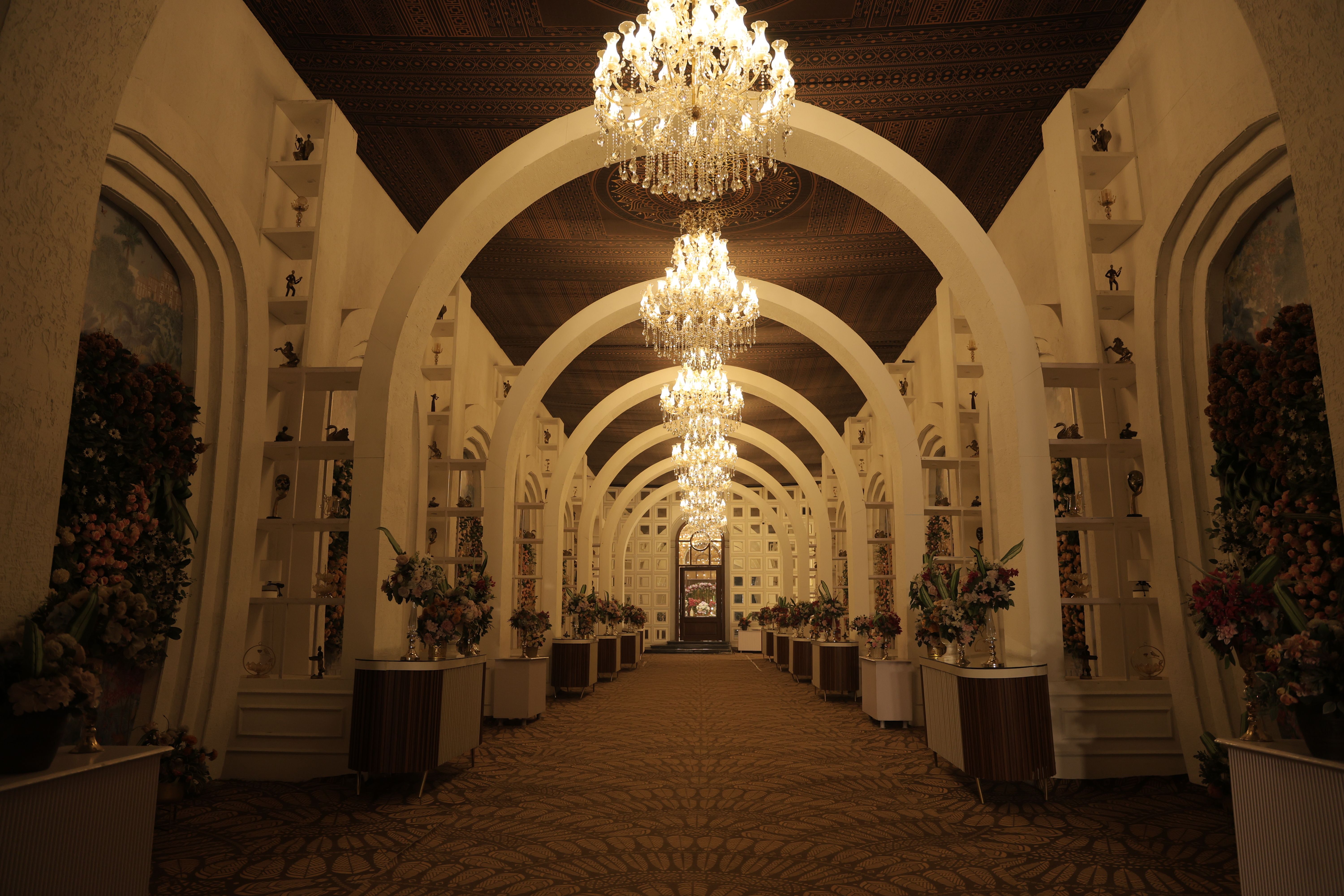 Elegant corridor with chandeliers and floral arrangements in a luxury venue.