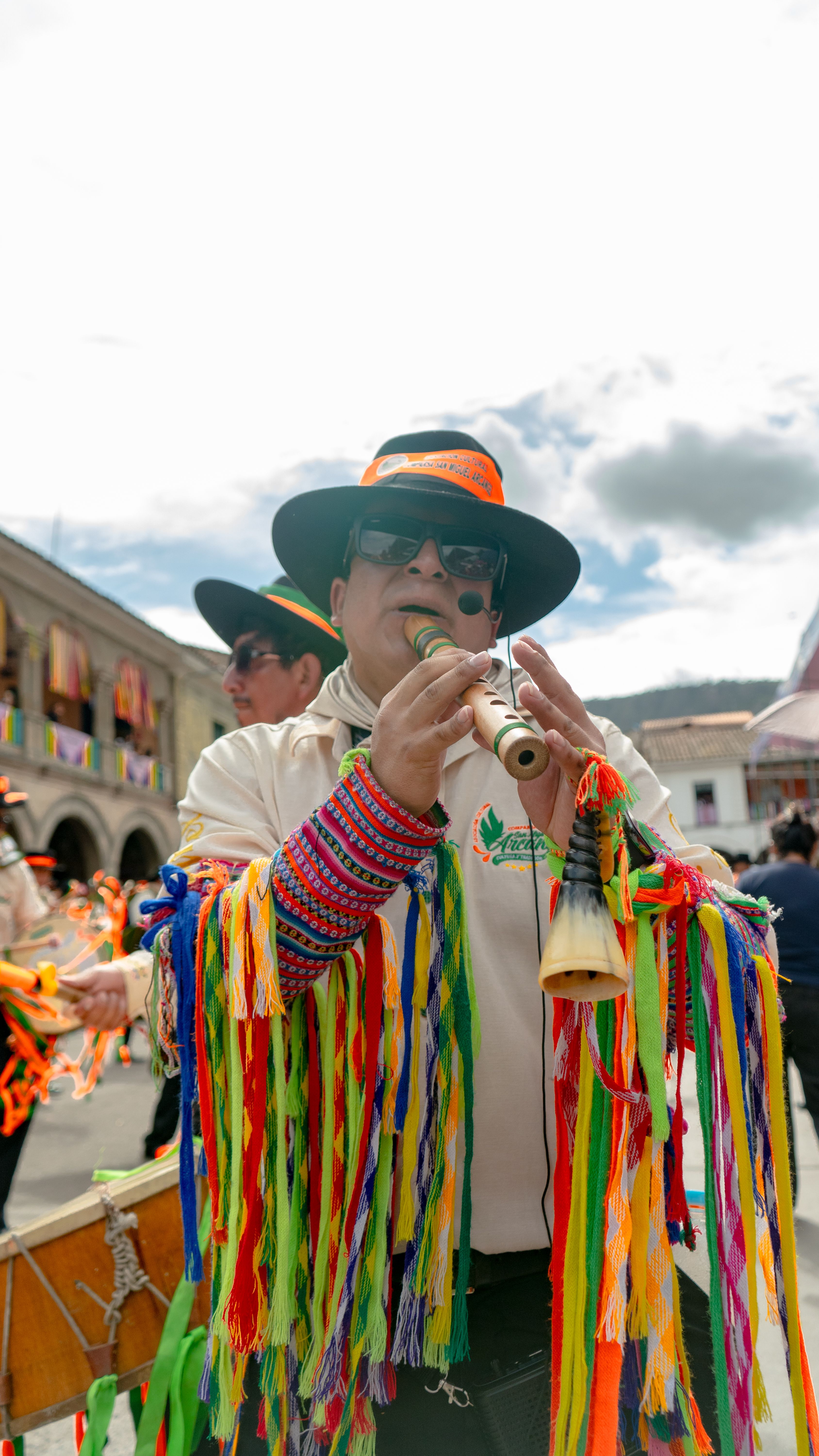 Man playing flute at vibrant outdoor festival in colorful traditional attire.