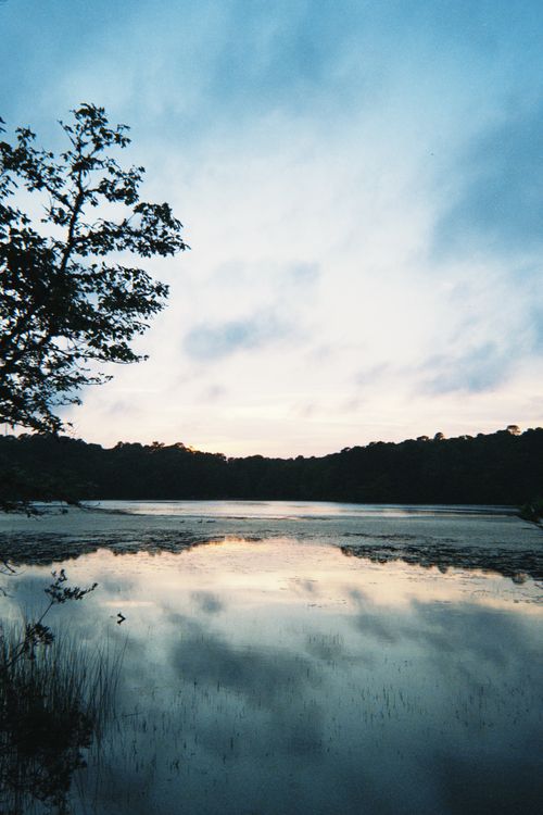 Free A tranquil lake at twilight reflecting the beautiful evening sky and surrounding trees. Stock Photo