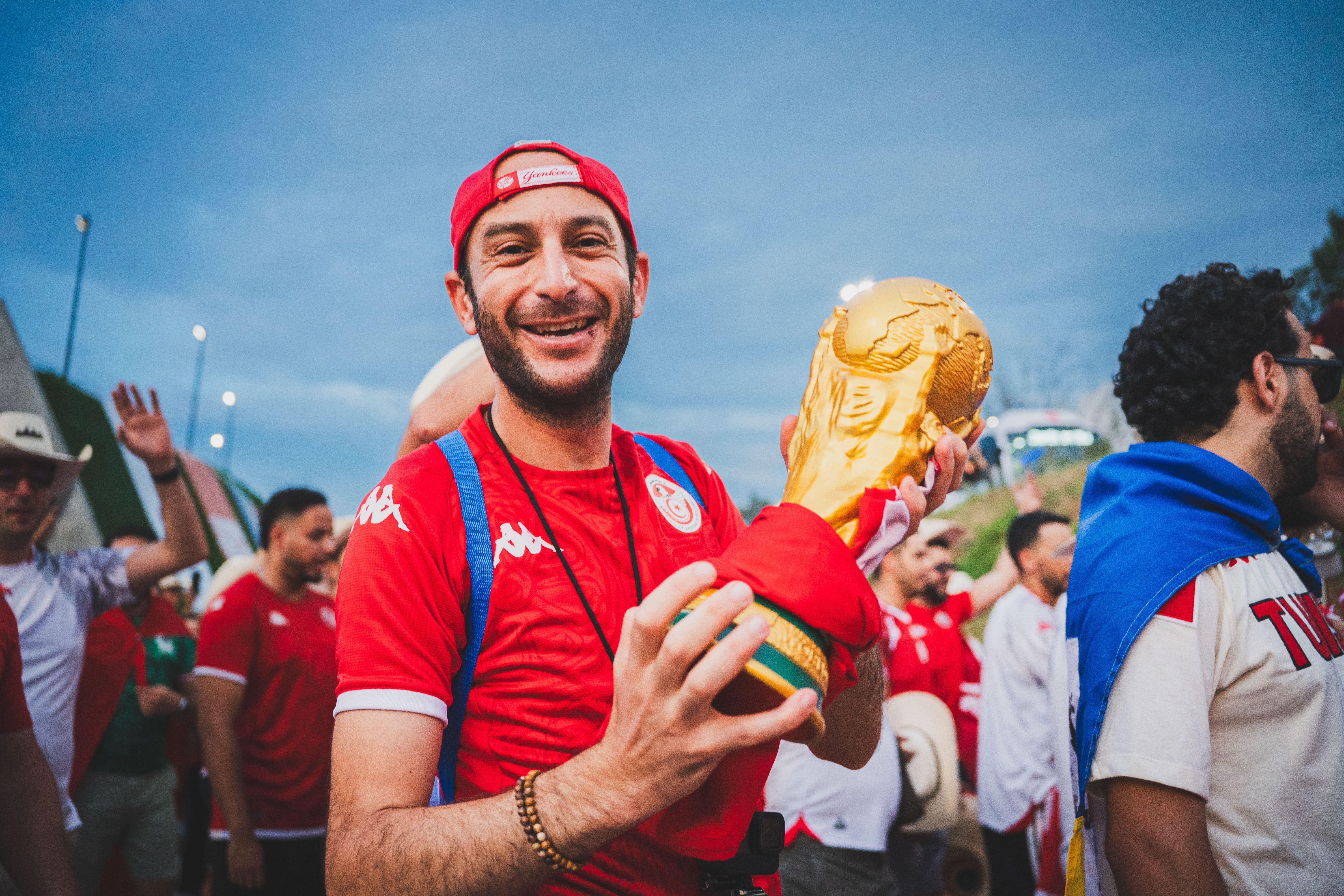 A happy soccer fan holding a trophy, surrounded by a vibrant crowd during a sports event.