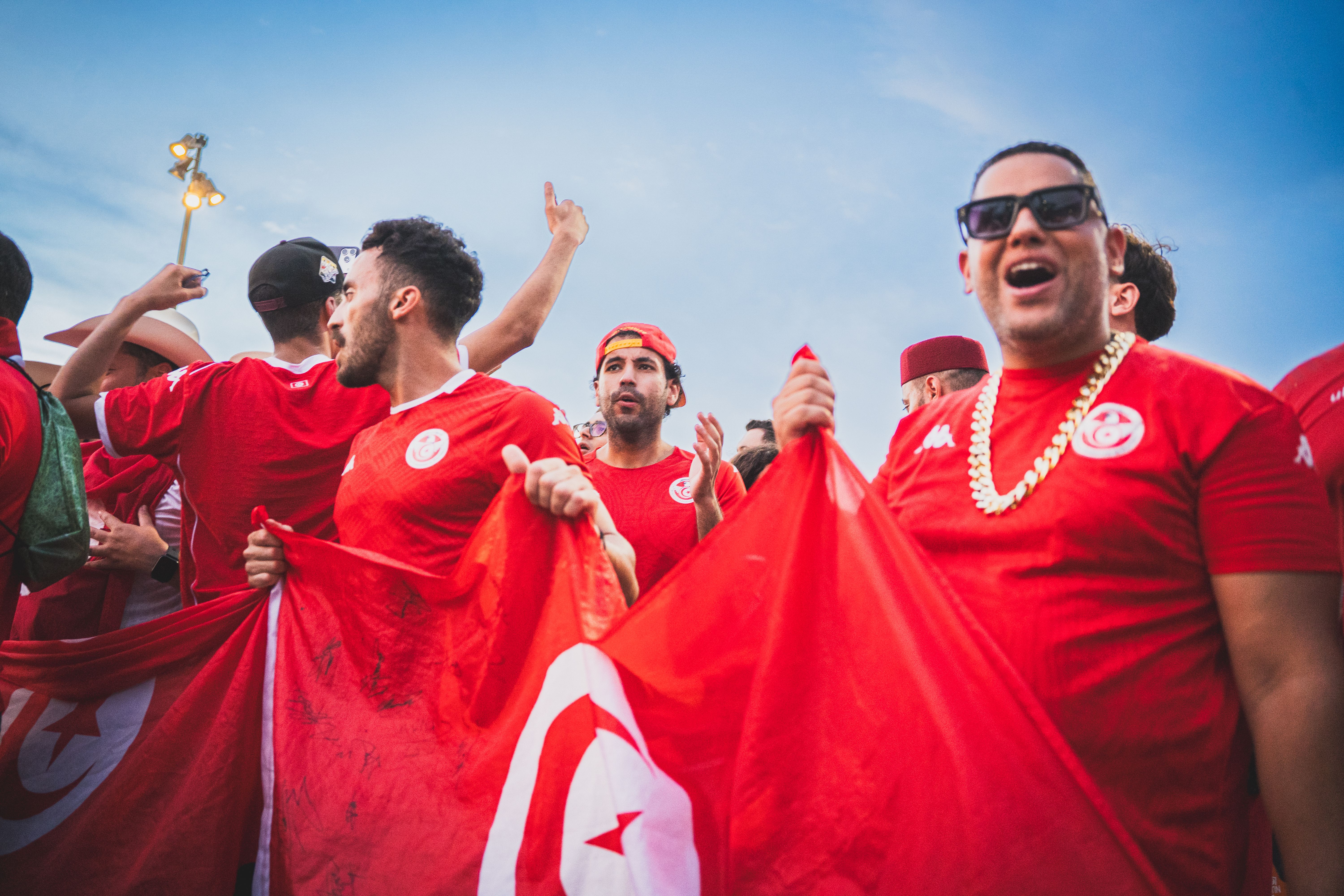 Excited soccer fans celebrating with Tunisian flags on a sunny day outdoors.