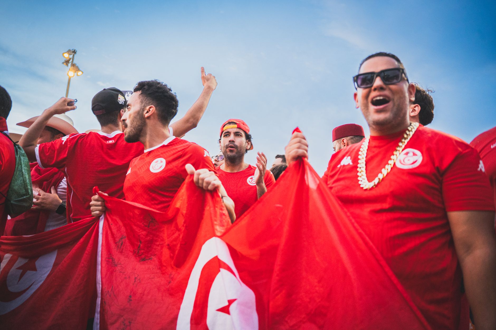Excited soccer fans celebrating with Tunisian flags on a sunny day outdoors.
