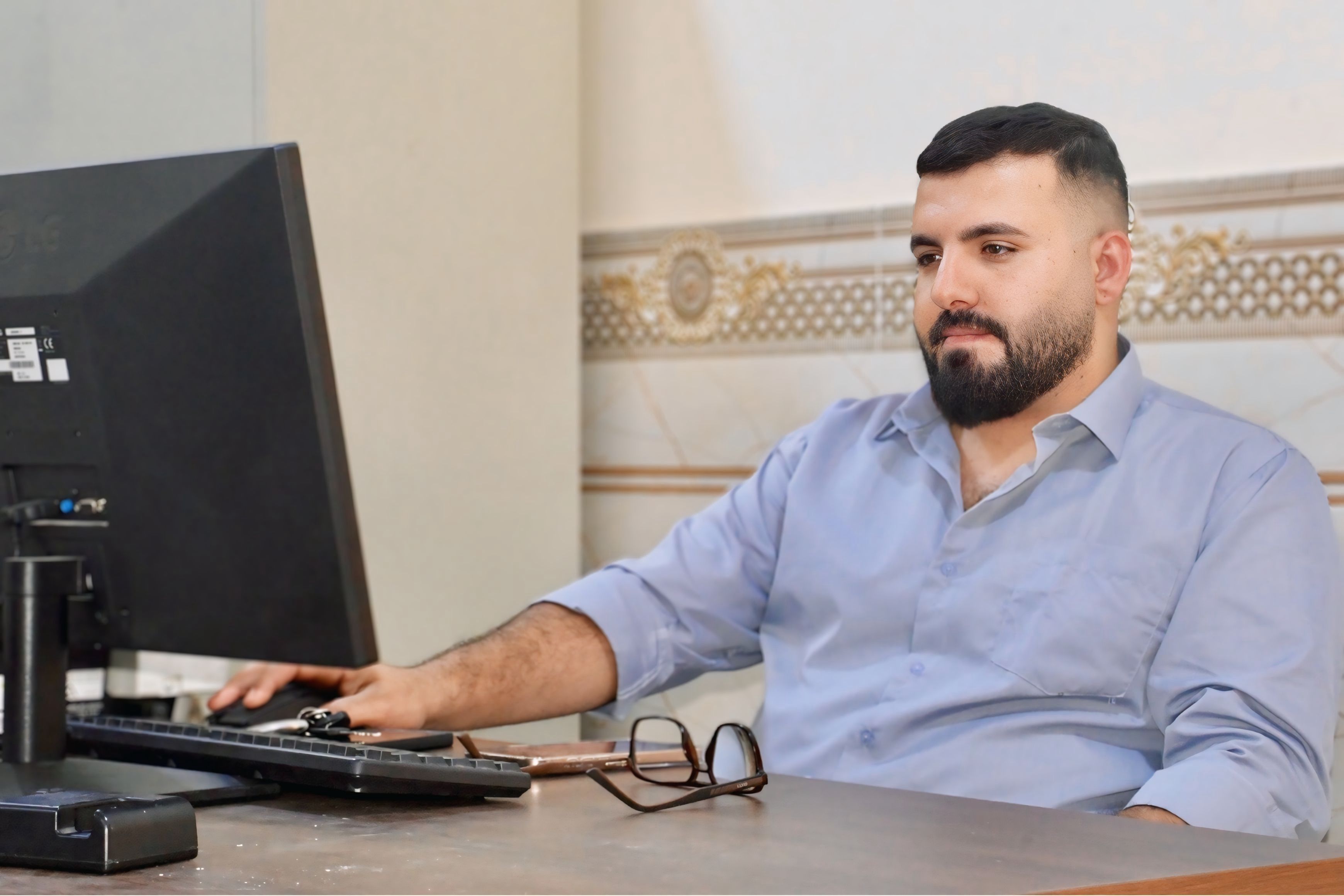 Man in office environment working on computer, casual outfit, focused.