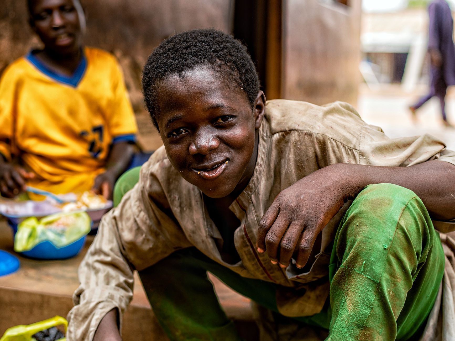 A joyful young boy smiling in a village setting with a blurred background.