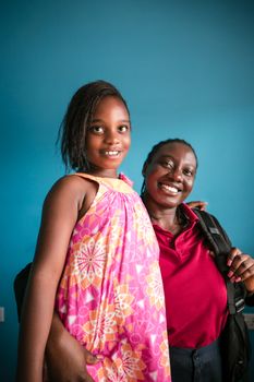 Happy mother and daughter smiling together in colorful attire indoors against a blue wall.