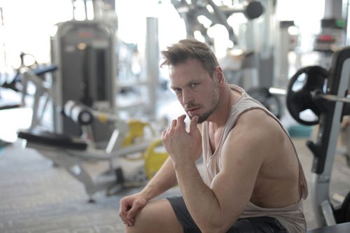 Free Confident young sportsman in sportswear sitting on bench and resting after workout in modern fitness center and looking at camera Stock Photo