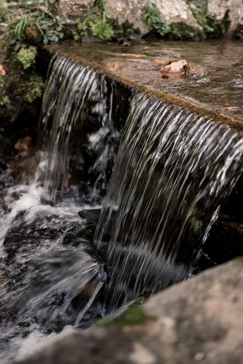 Free A serene waterfall flowing over rocks surrounded by lush greenery, evoking tranquility. Stock Photo