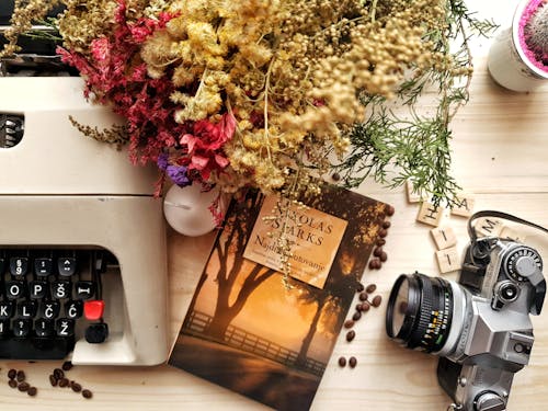 ヴィンテージタイプライターとカメラで木製のテーブルに配置された花と本の束