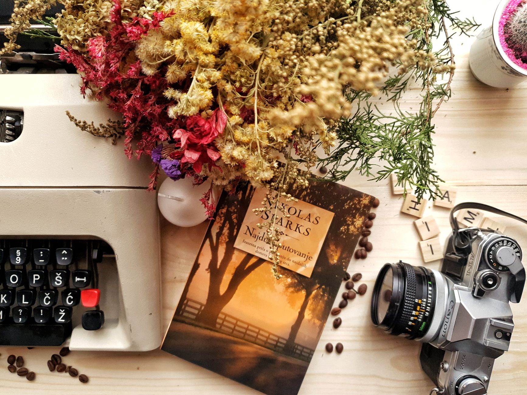 A cozy vintage workspace featuring a typewriter, camera, book, and dried flowers.