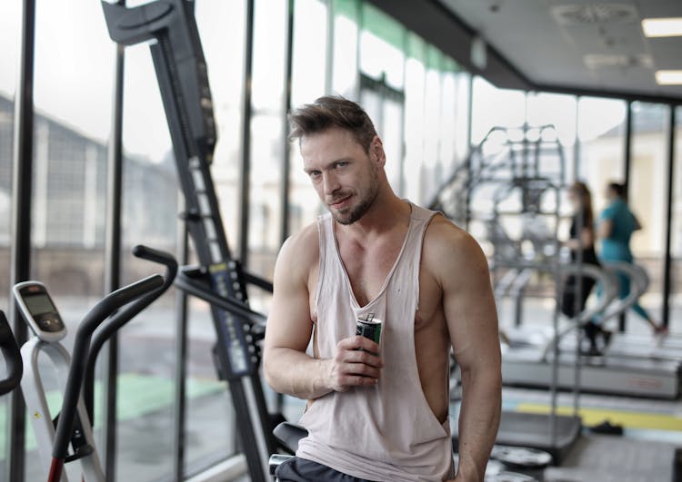 Young Muscular Male Athlete Resting After Workout And Drinking Energy Drink In Modern Gym