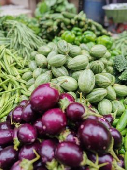 A vibrant assortment of fresh vegetables including brinjals and cucumbers at a local market stall.