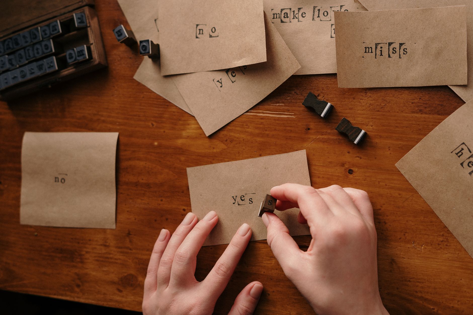 Hands creating letterpress art with vintage stamps on brown paper cards.