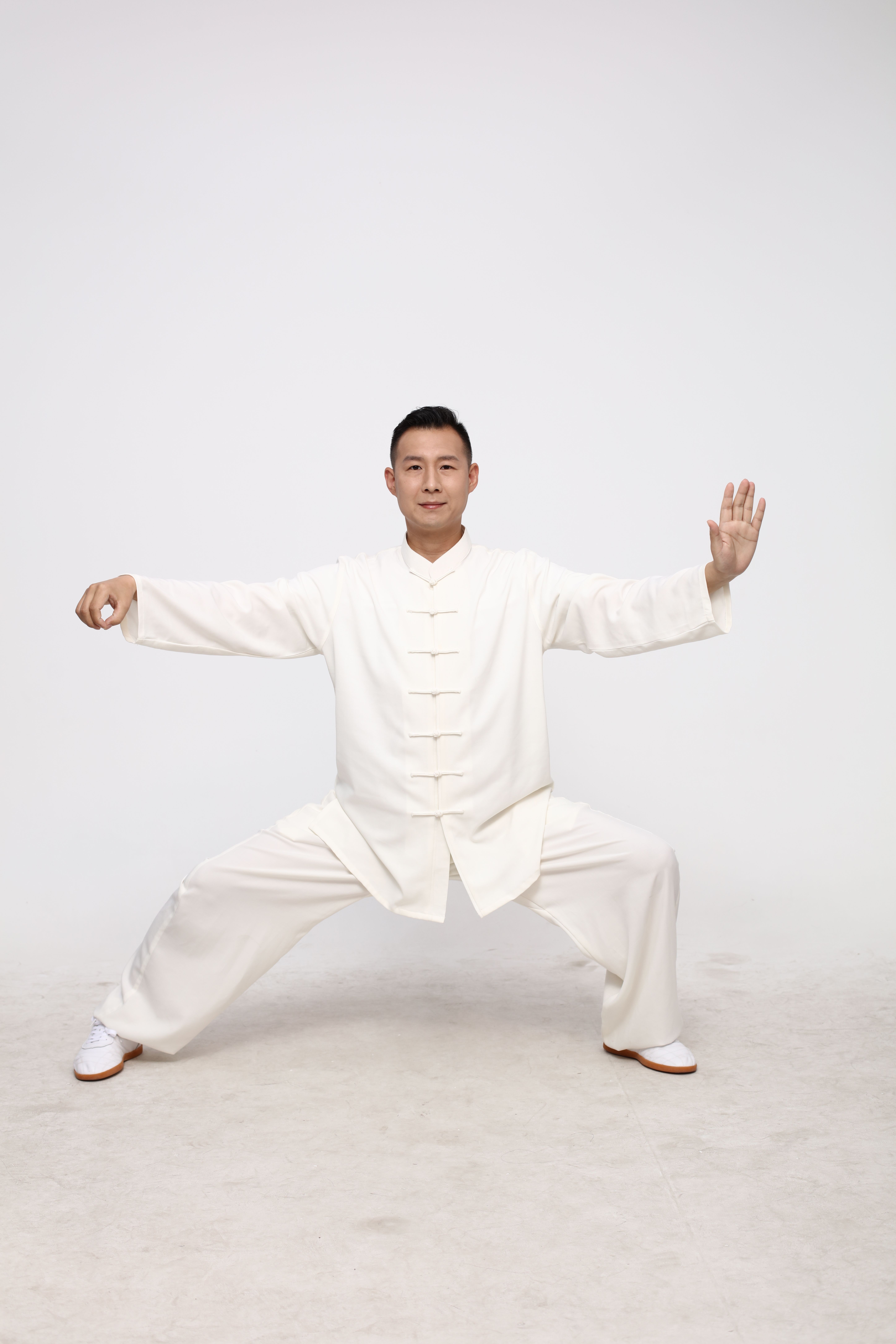 Young man in traditional Tai Chi pose wearing a white martial arts uniform on a neutral background.