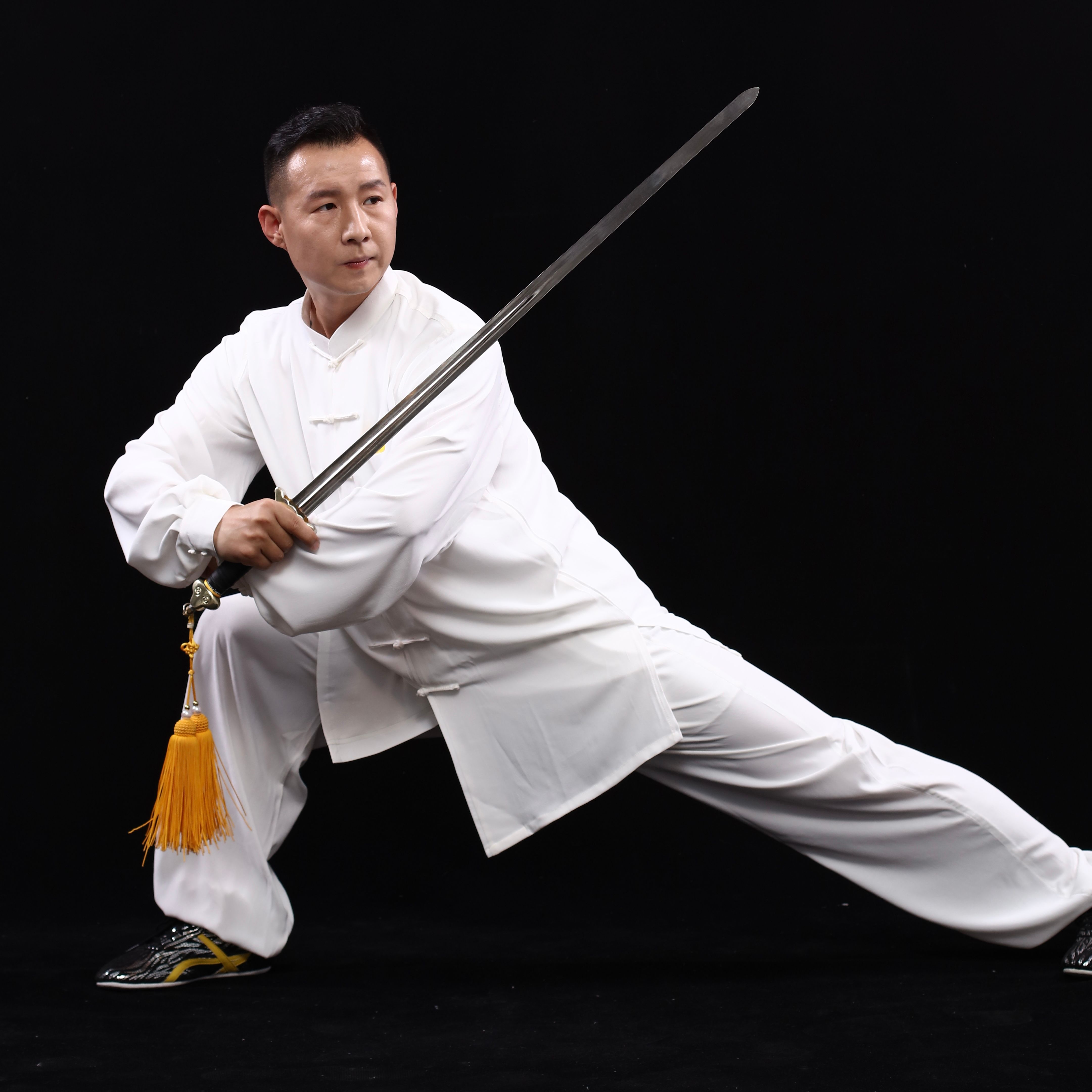 Martial artist demonstrating skillful sword technique in traditional white attire against a black background.