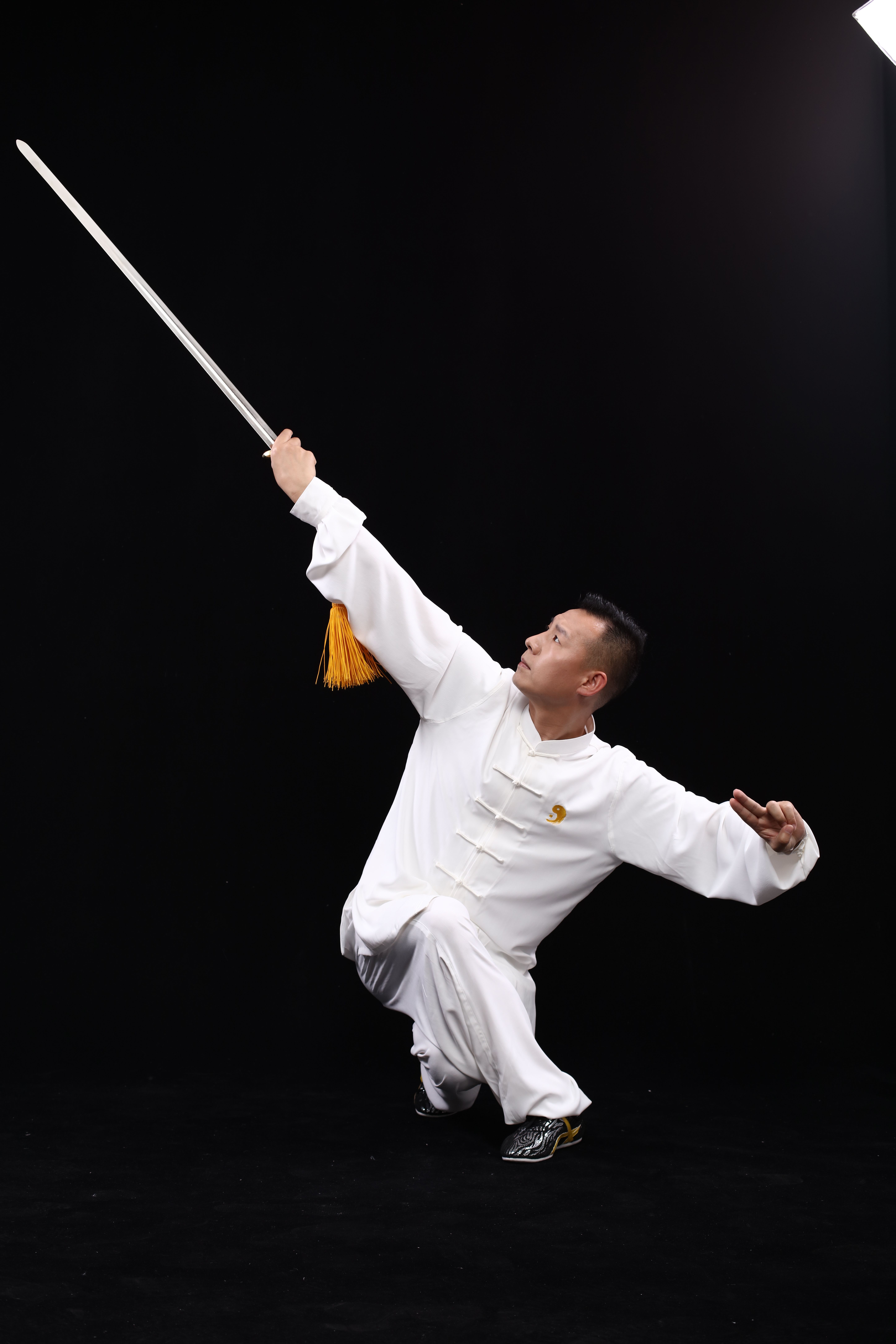 Martial artist demonstrates skill with a sword in a dynamic pose indoors.