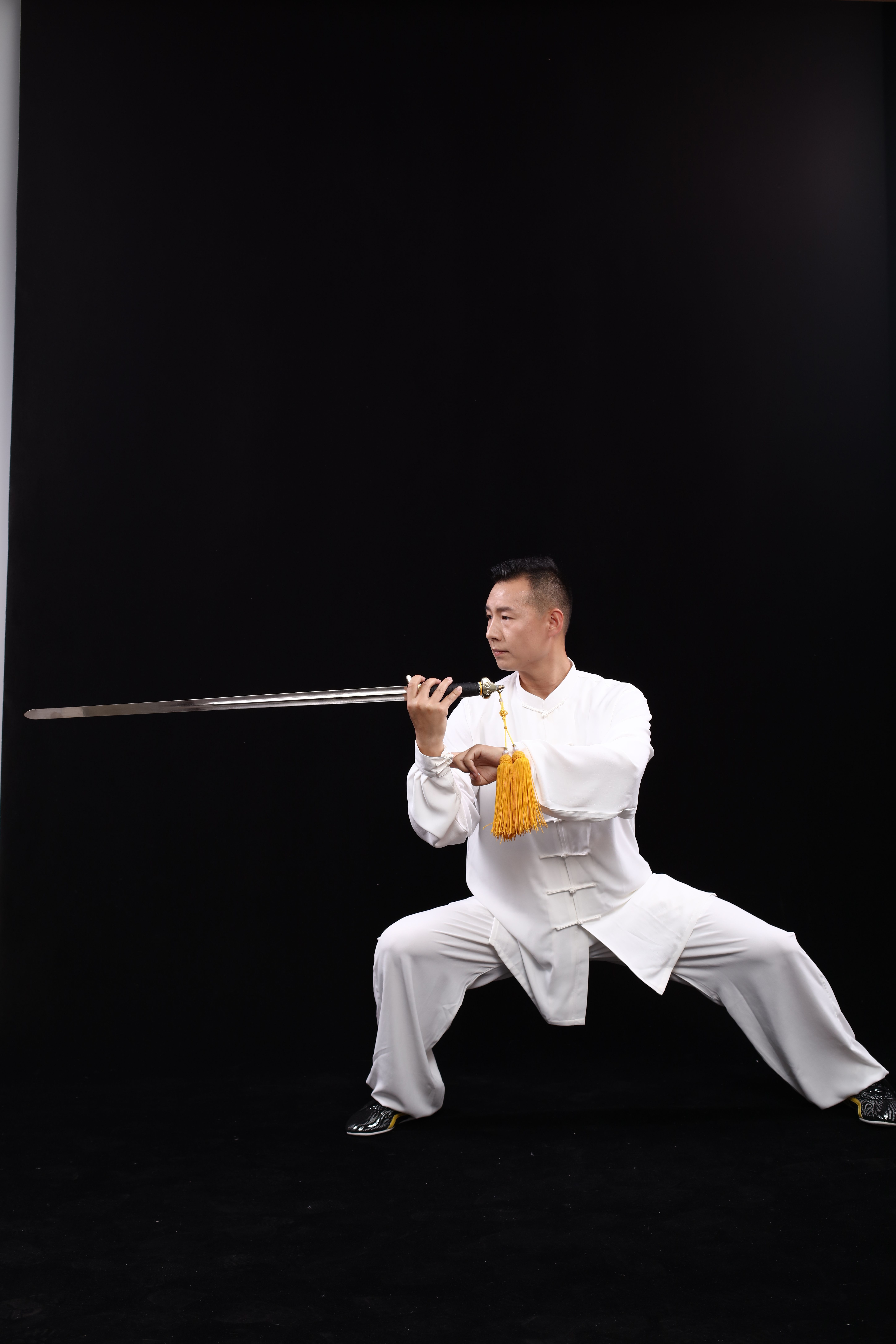 Martial artist performing a traditional sword pose in studio.