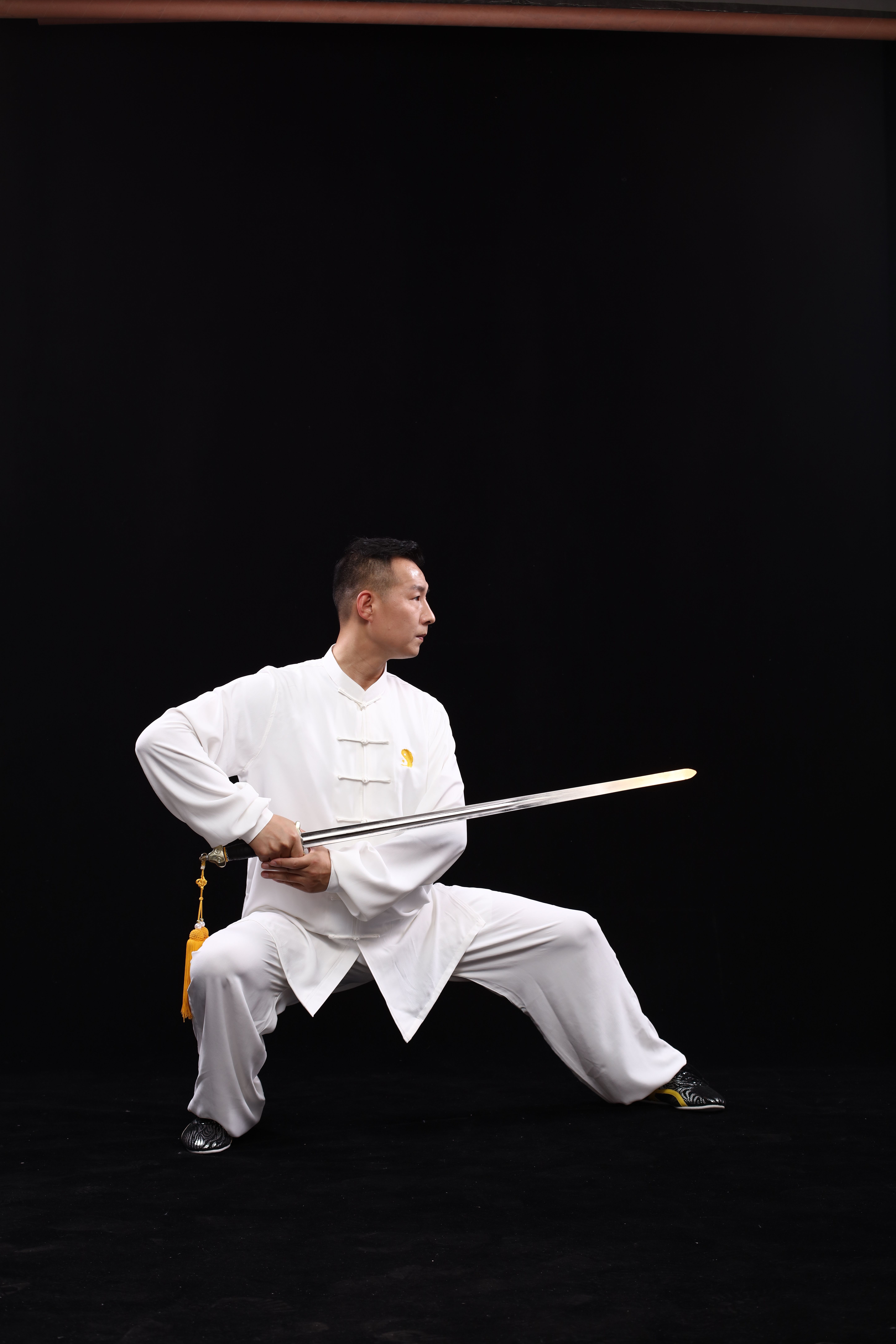 Martial artist in classic white attire performs a kung fu pose with a sword against a black background.