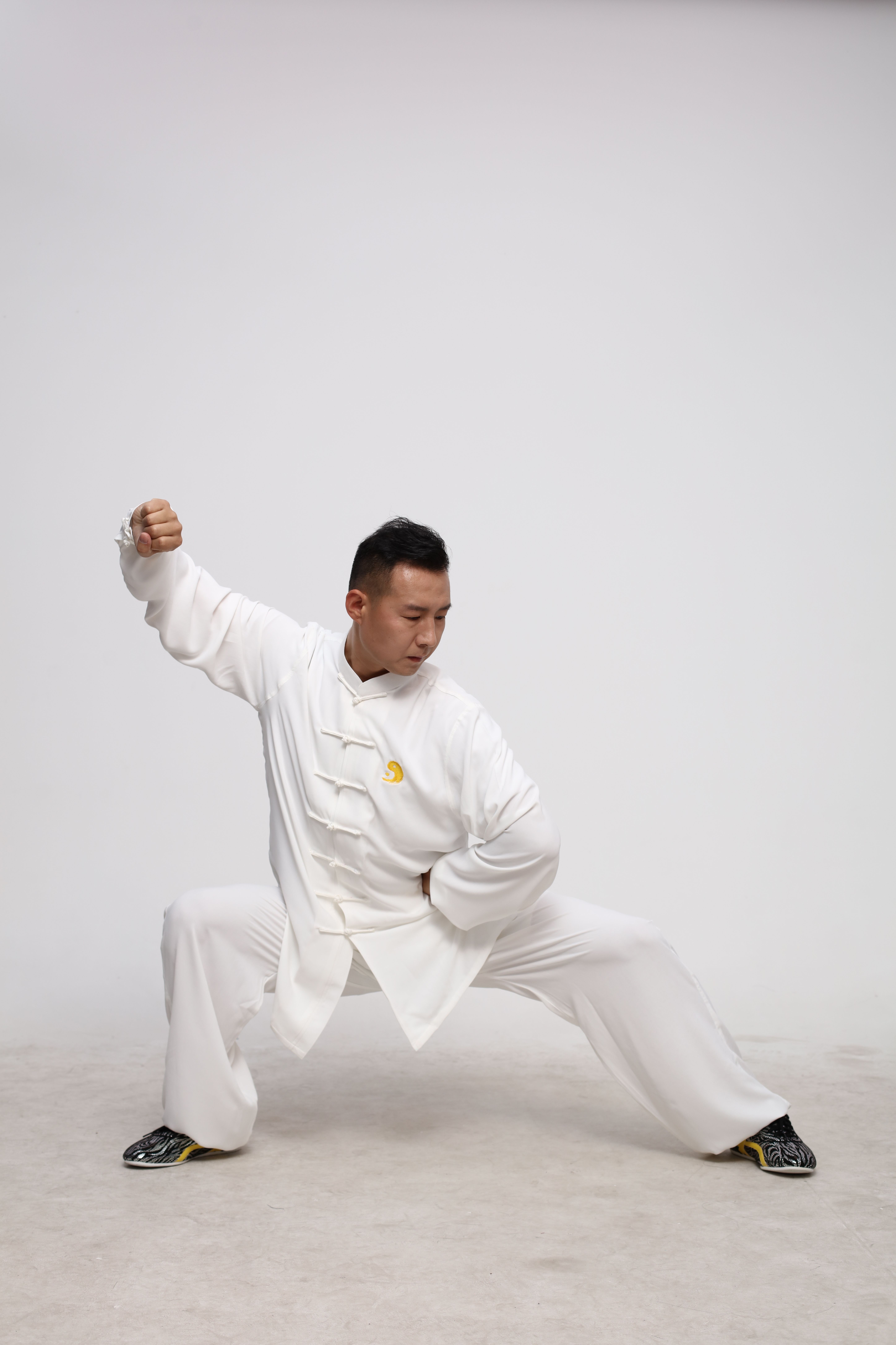 A martial artist demonstrating a Tai Chi pose indoors, dressed in traditional white attire, conveying calmness and focus.