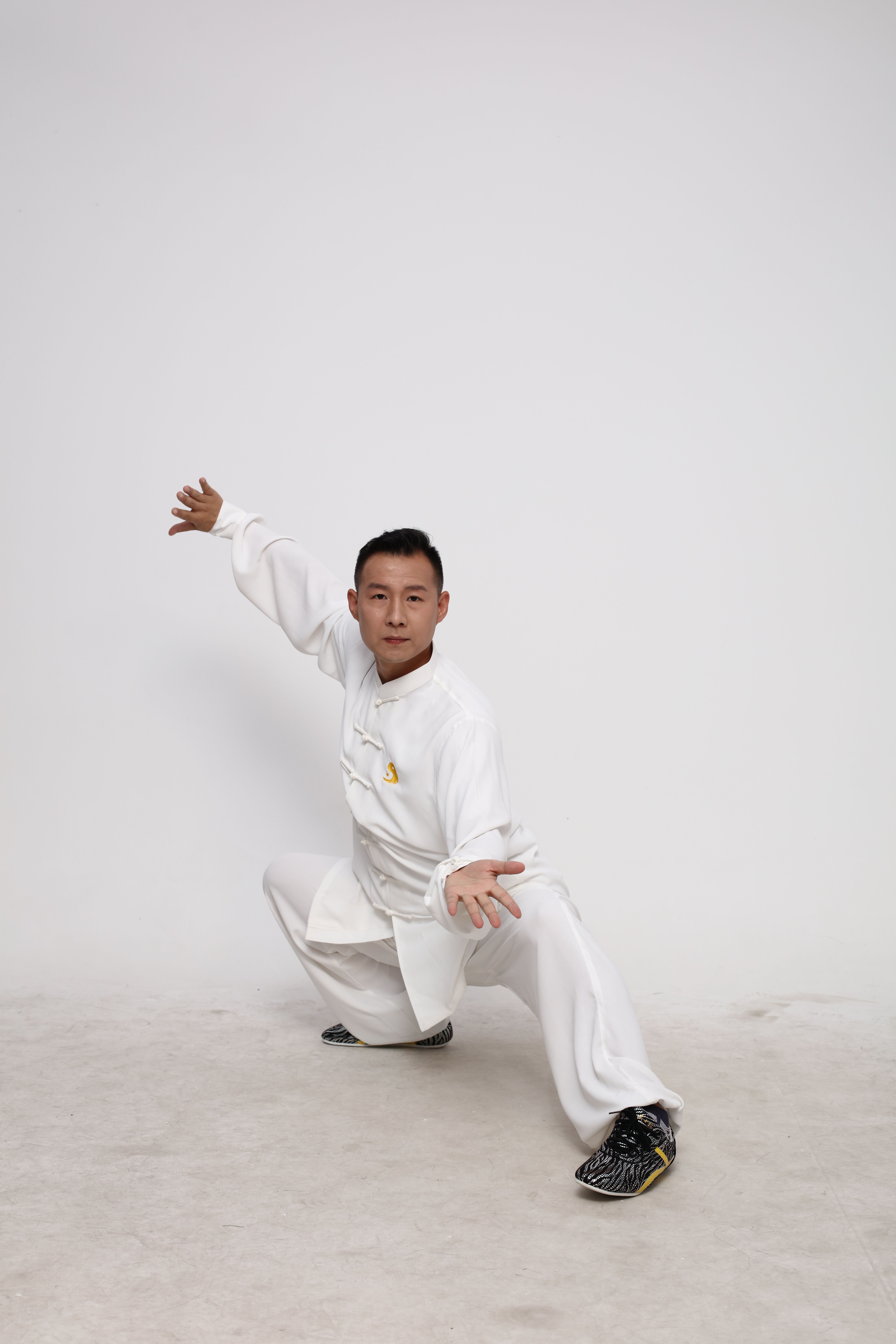A martial artist demonstrating a traditional pose in a white uniform against a plain background.