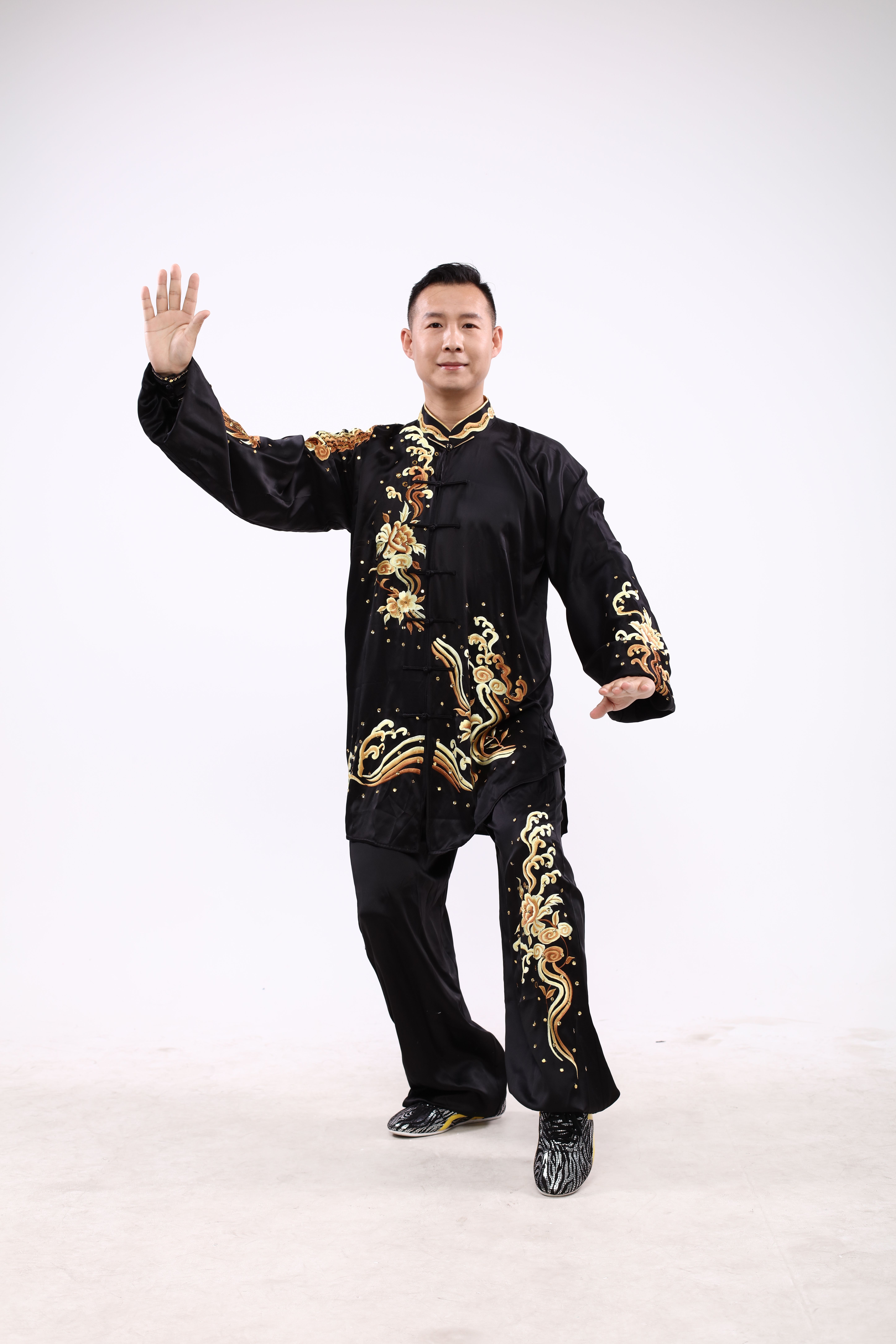 Martial artist in black and gold traditional costume posing gracefully indoors.