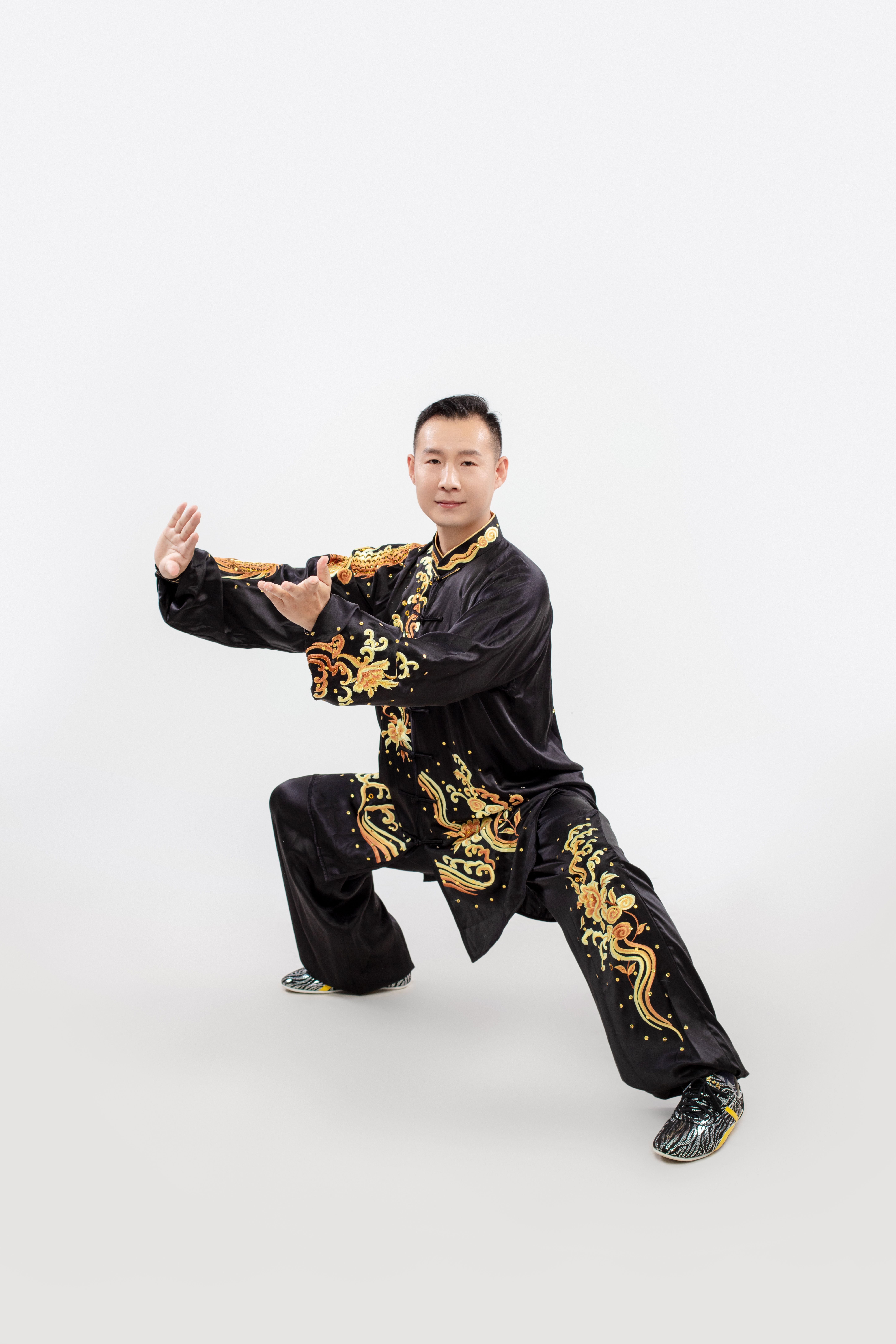 Martial artist in a dynamic pose wearing a traditional black robe with dragon motifs on a white background.