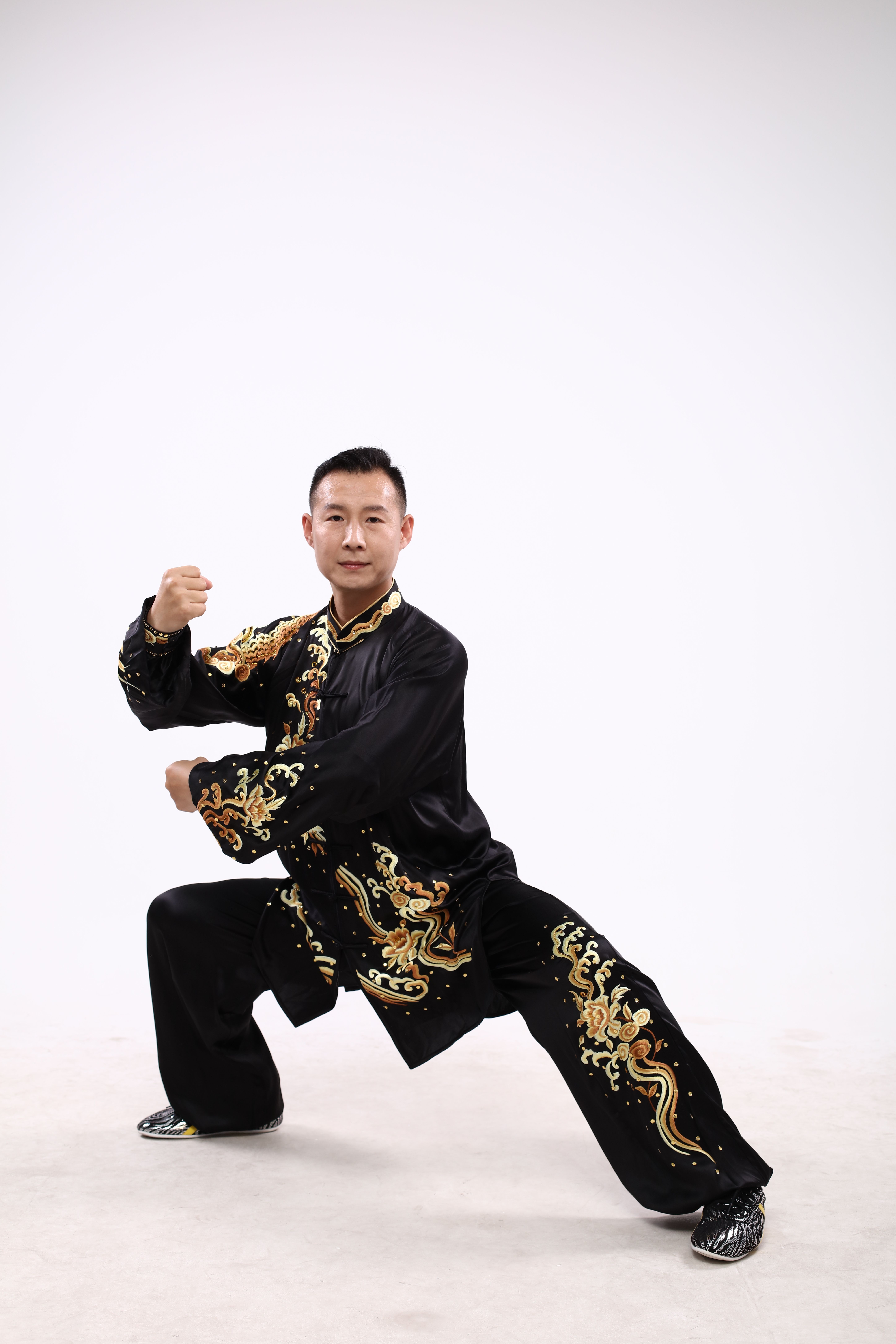 Martial artist posing in intricate traditional Chinese costume on a neutral background.