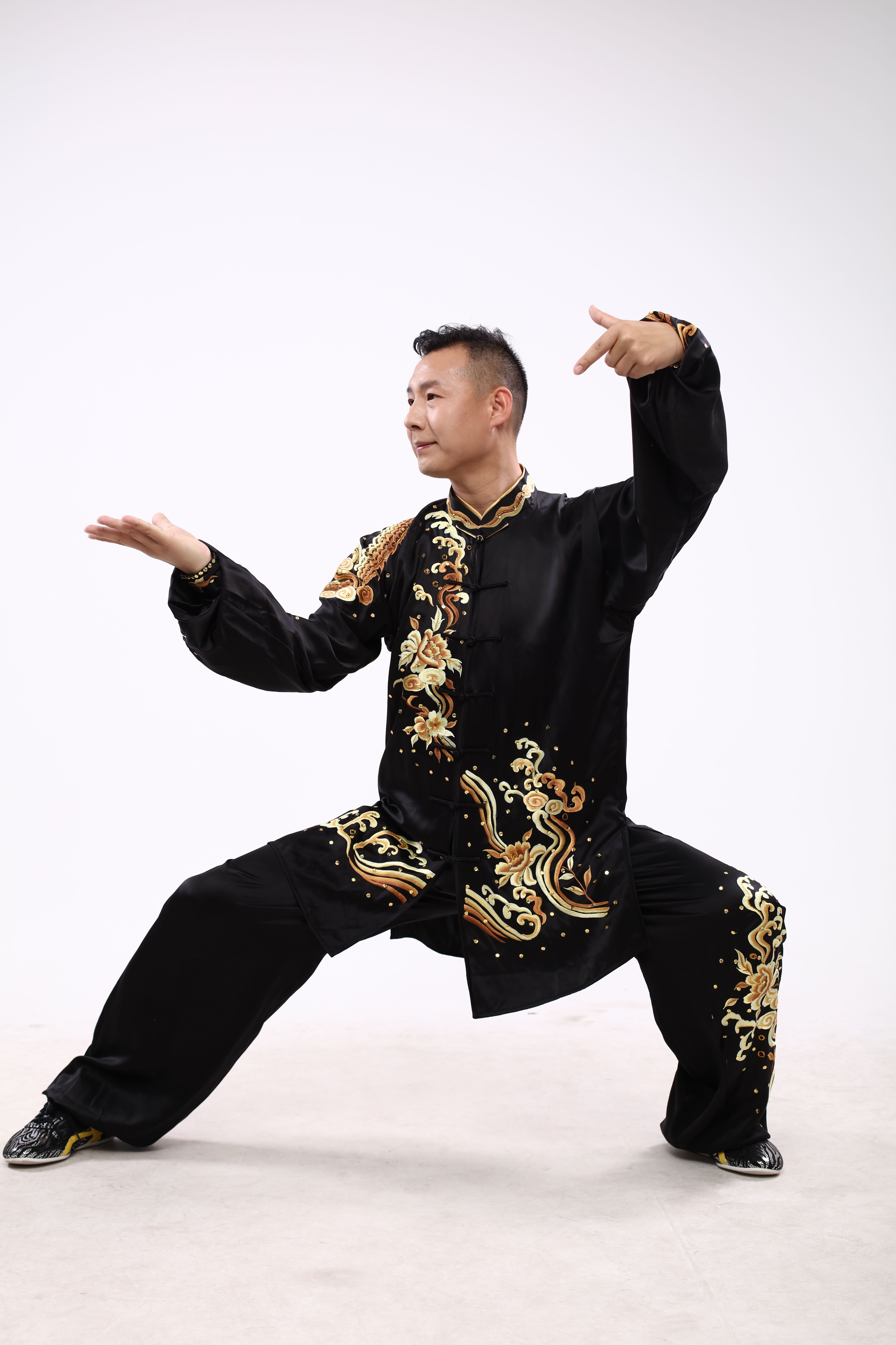 Martial artist in traditional attire striking a Wushu pose against a white backdrop.