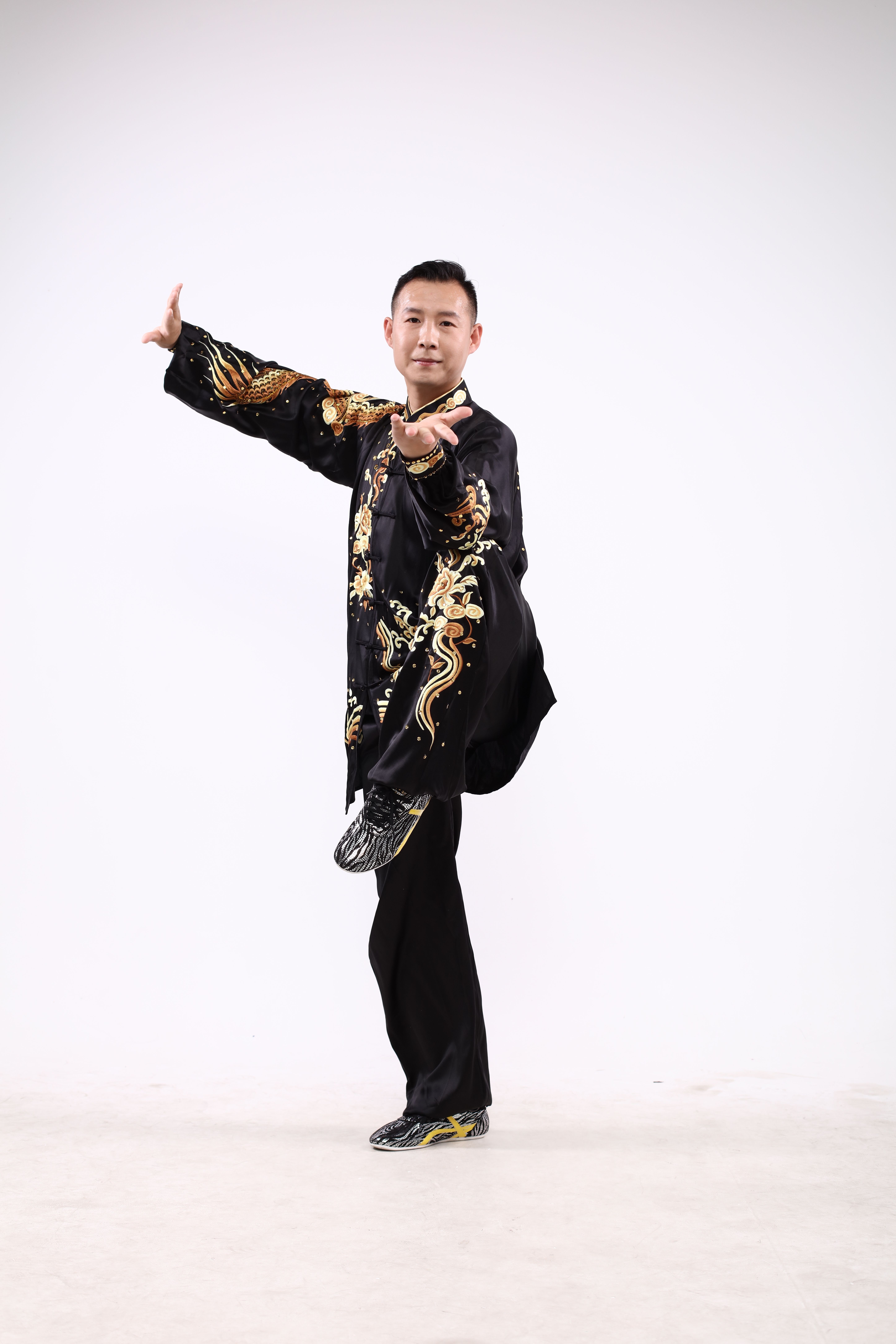 Martial artist performing a high kick while wearing traditional decorative attire on a white background.
