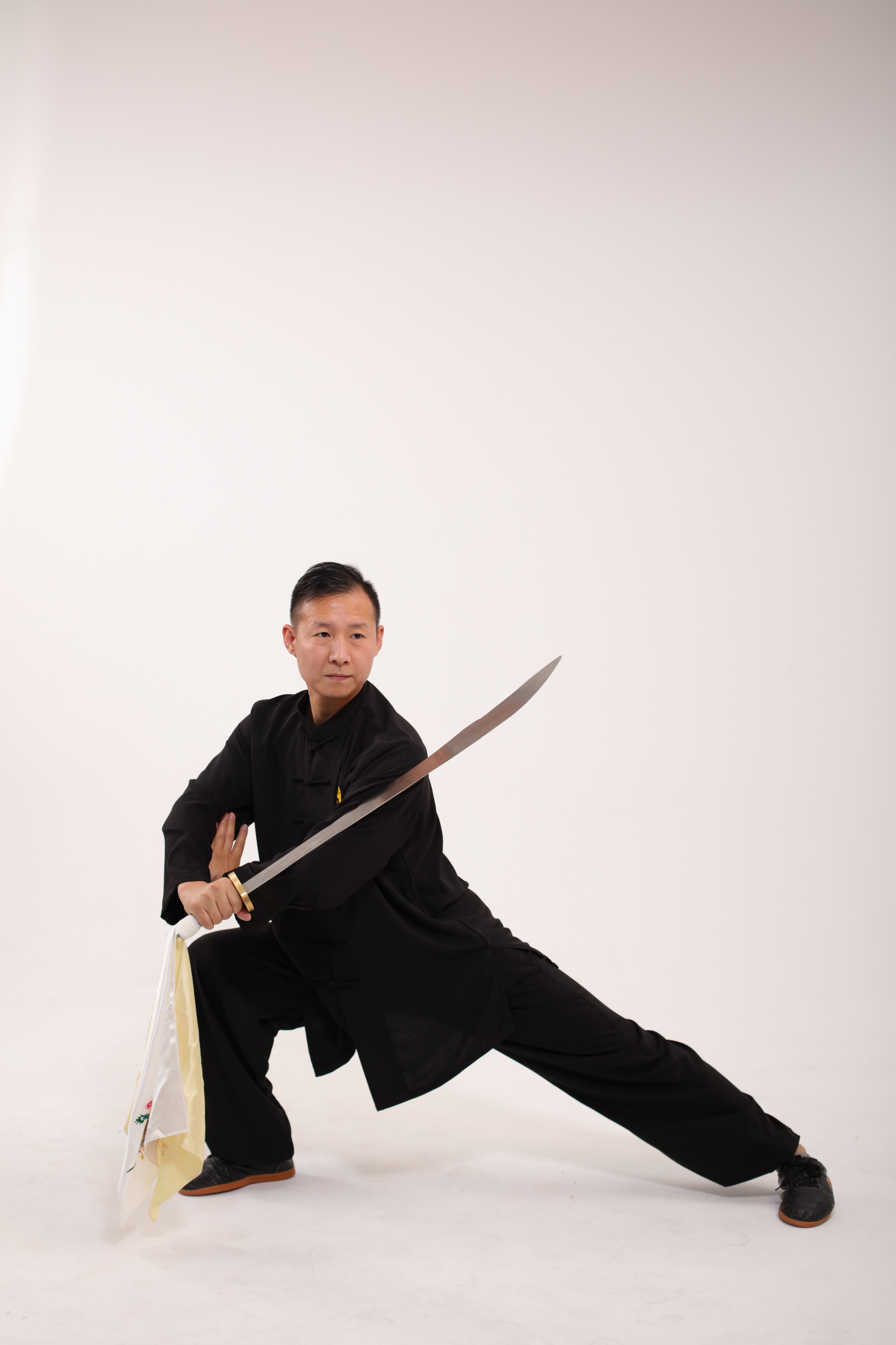 Martial artist in black attire performing a sword pose against a plain studio background.
