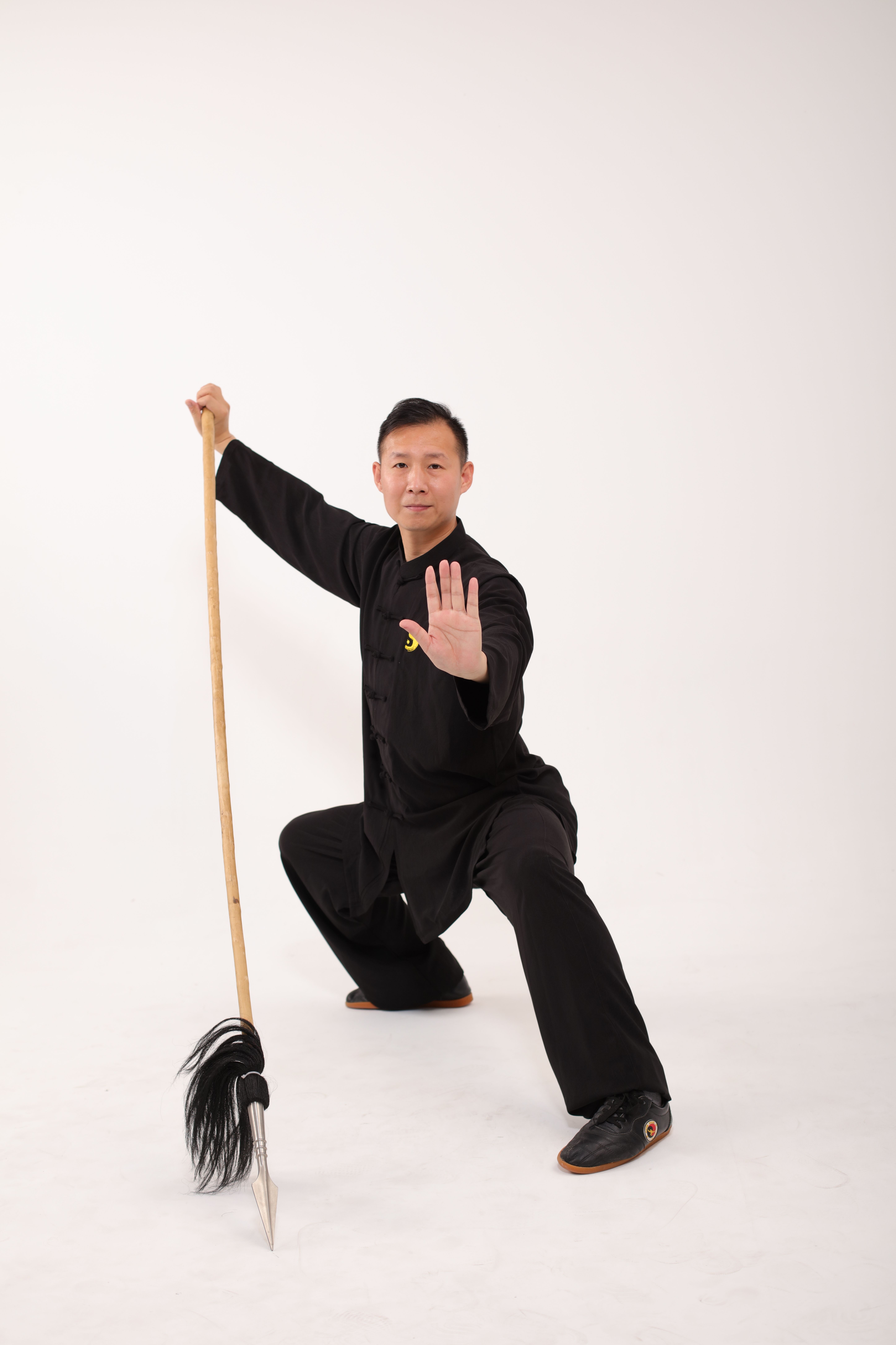 Martial artist performs kung fu pose with traditional weapon in studio.