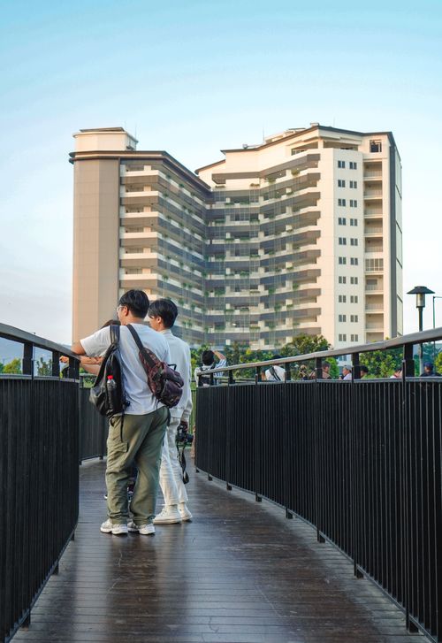Free Two people walking on a bridge with a modern apartment building in the background, capturing daily urban life. Stock Photo